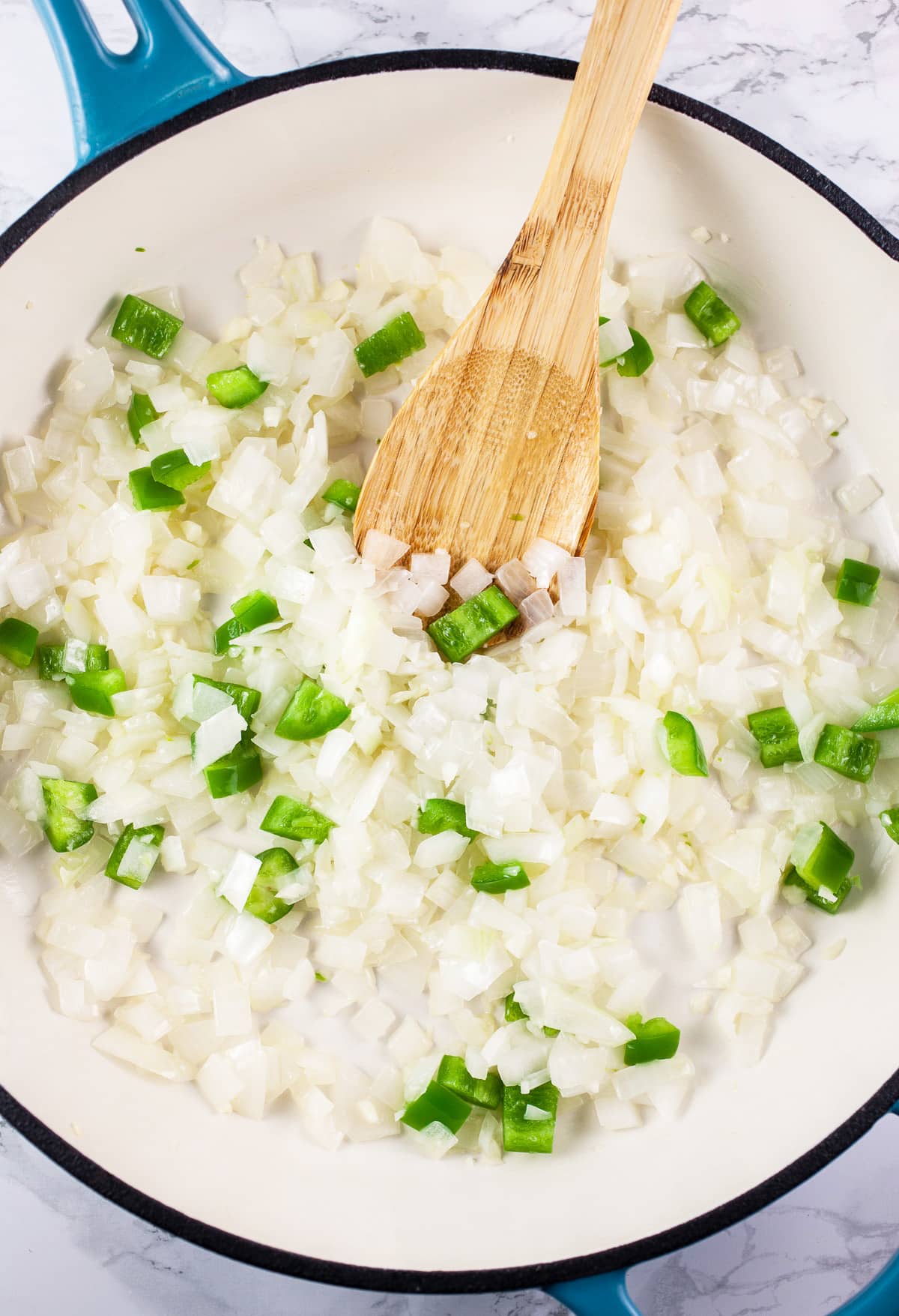 Minced garlic, onions, and jalapenos sautéed in skillet with wooden spoon.