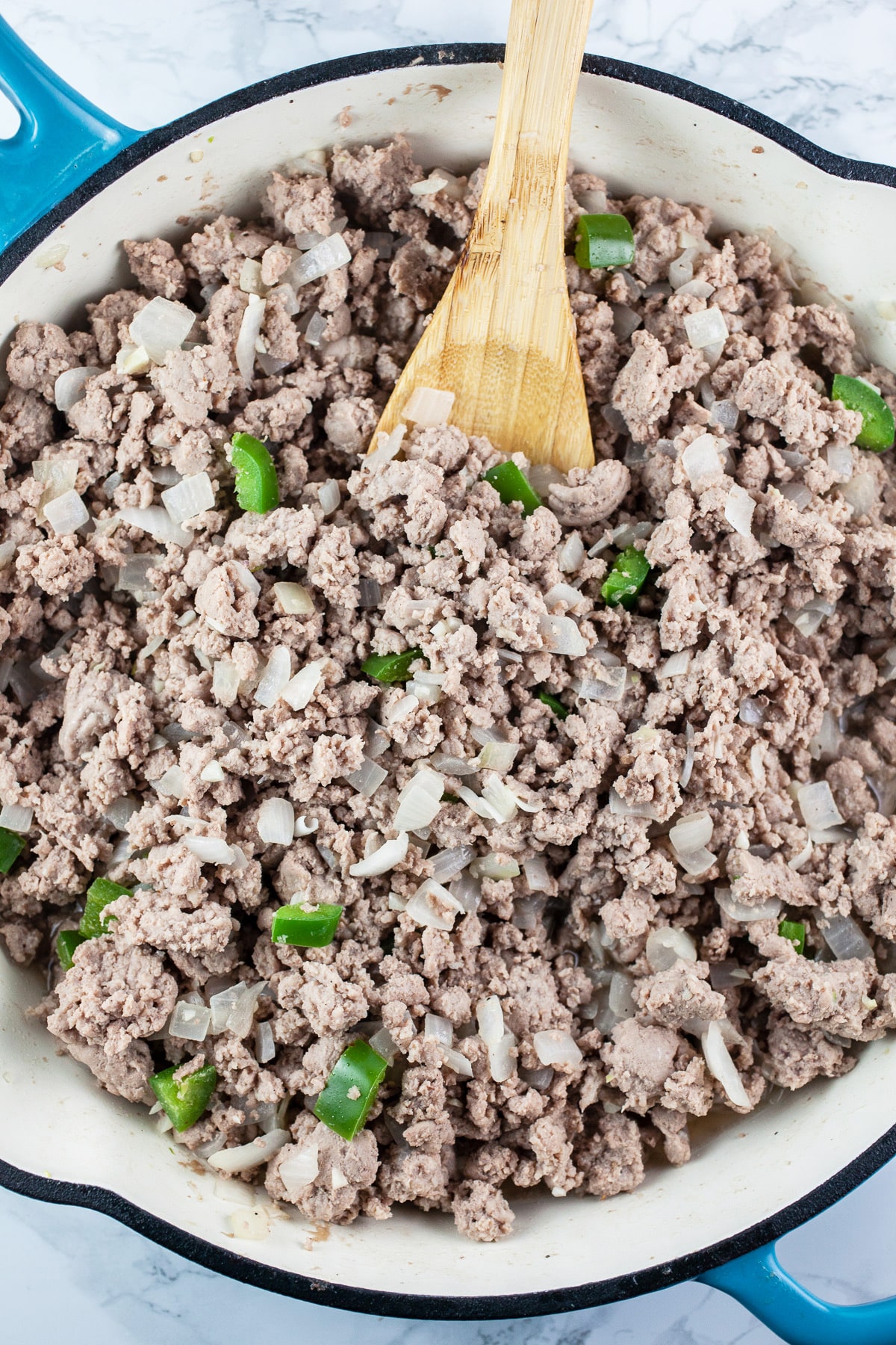 Ground turkey sautéed with minced garlic, onions, and jalapeno peppers in skillet with wooden spoon.