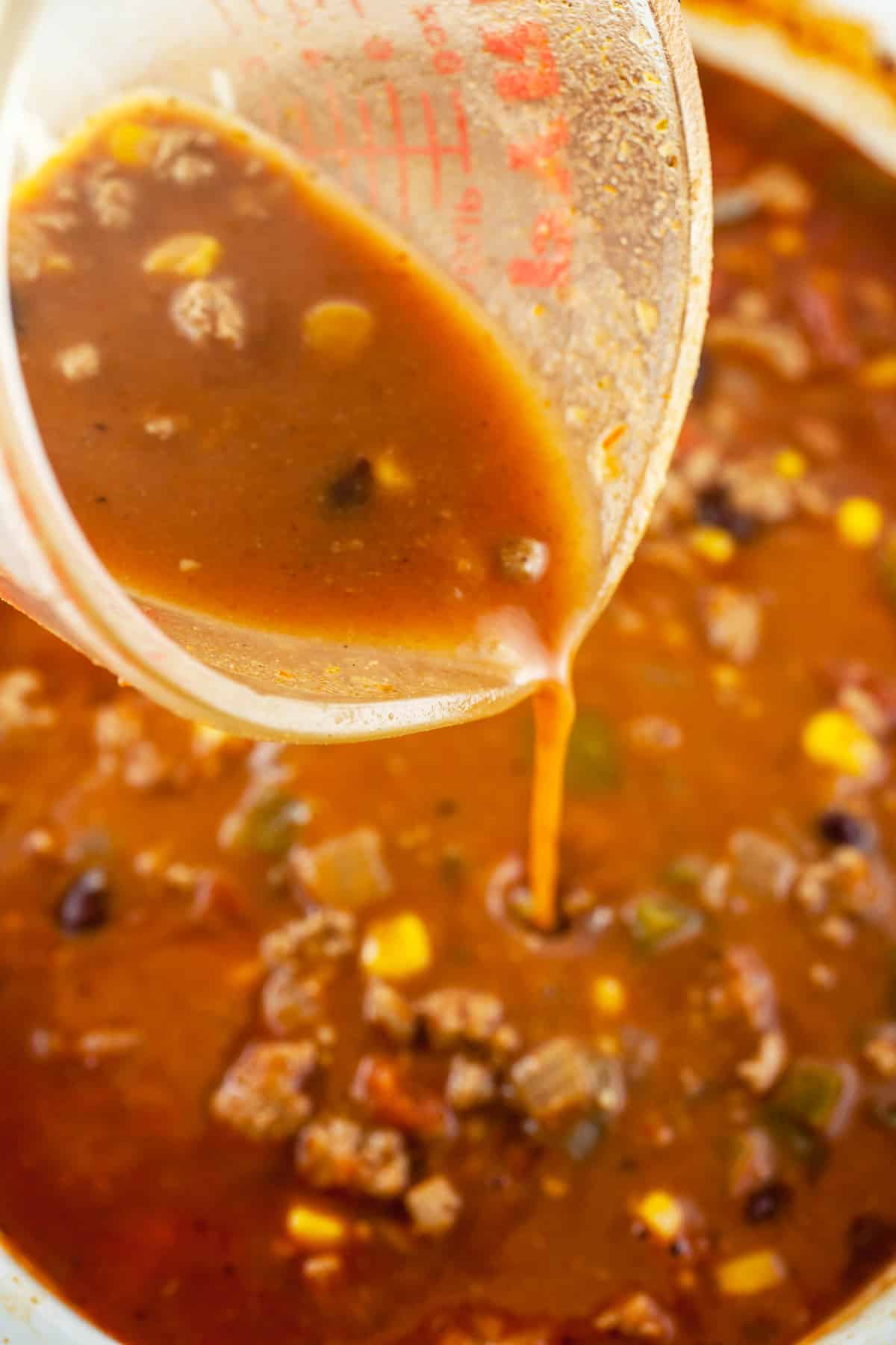 Cornstarch slurry poured into turkey chili from glass measuring cup.