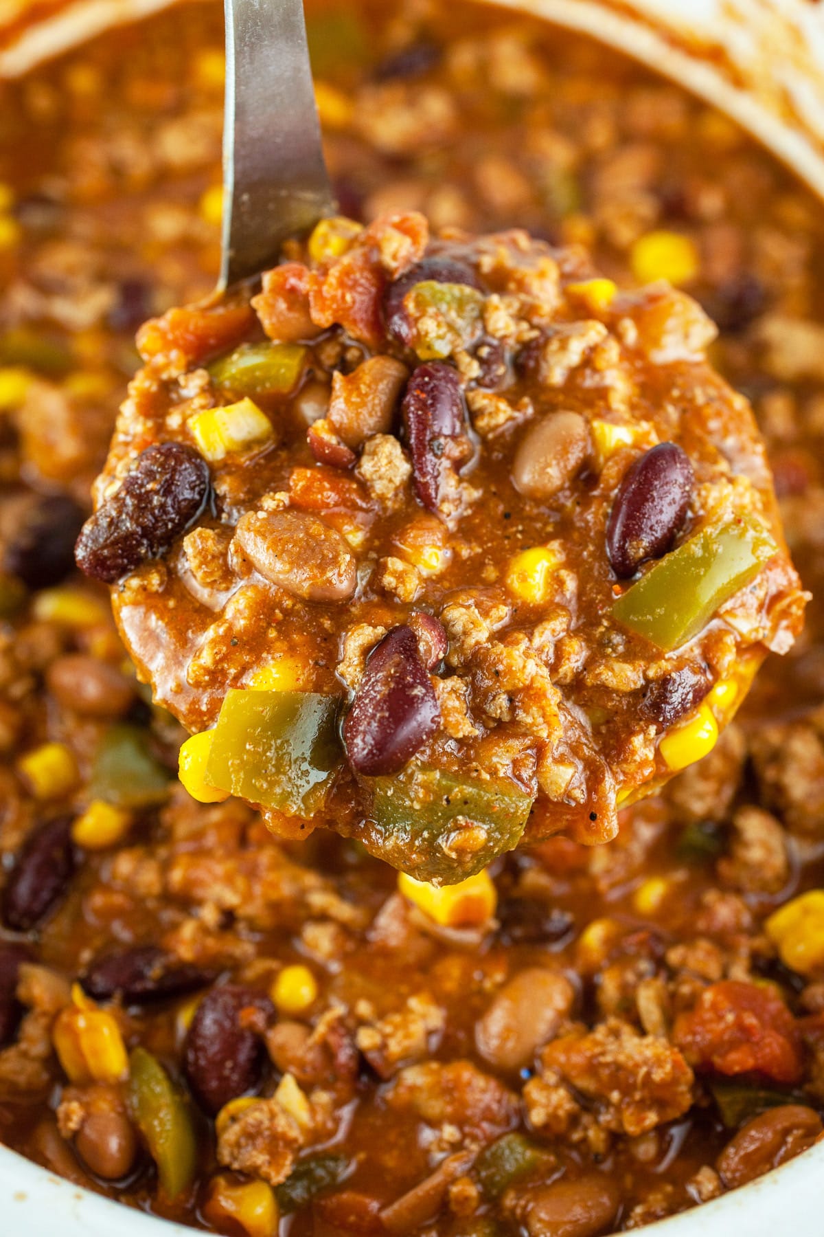 Scoop of turkey chili lifted from slow cooker on metal ladle.