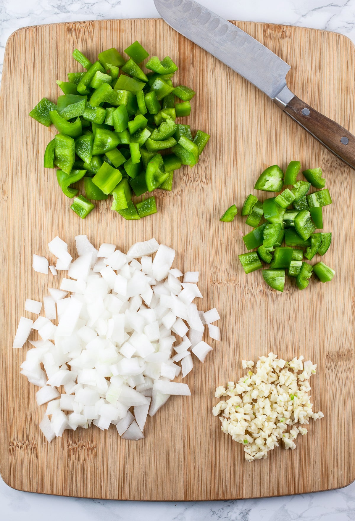 Minced garlic, onions, jalapeno, and bell peppers on wooden cutting board with knife.