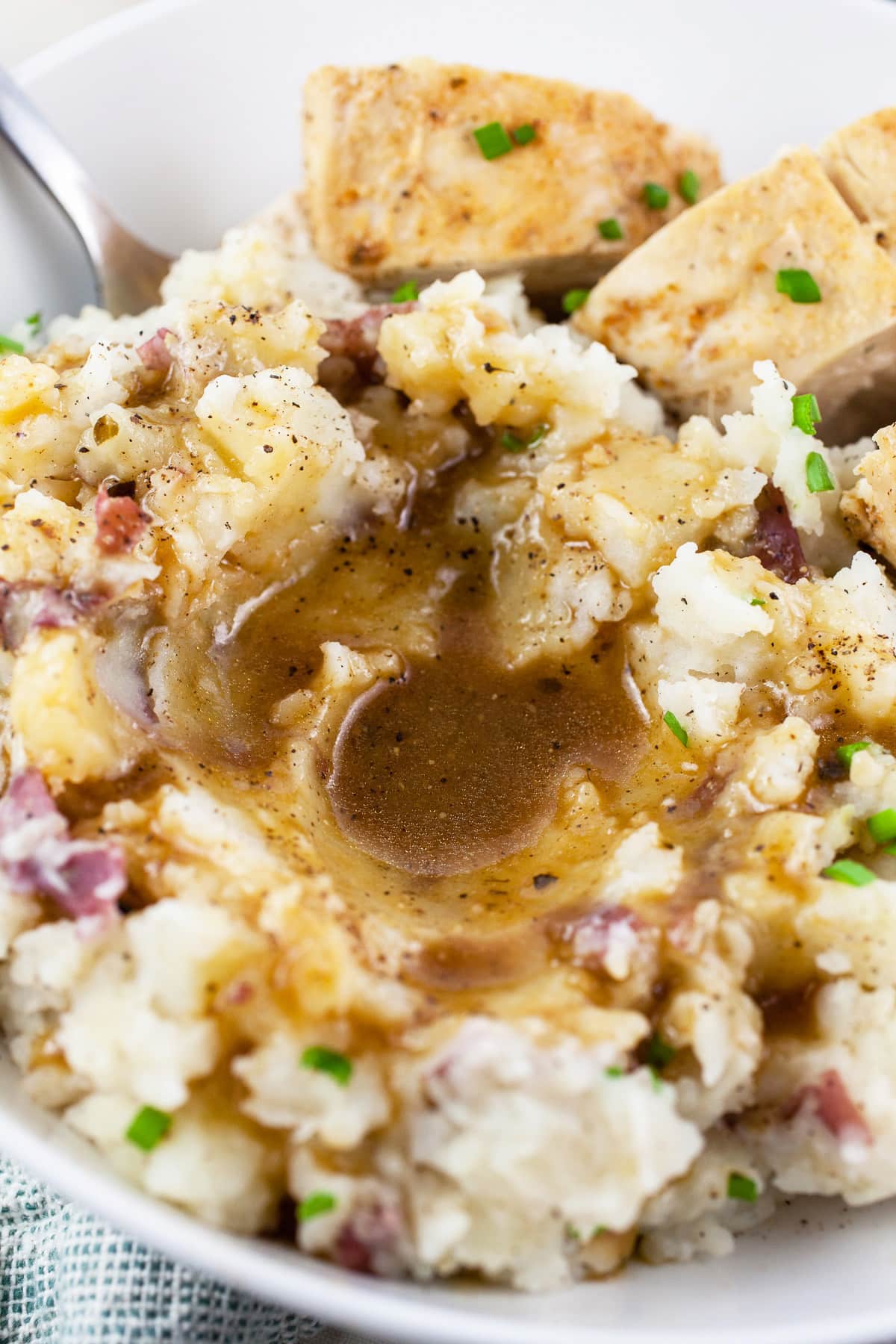 Mashed red potatoes with gravy and chicken breast in white bowl with fork.