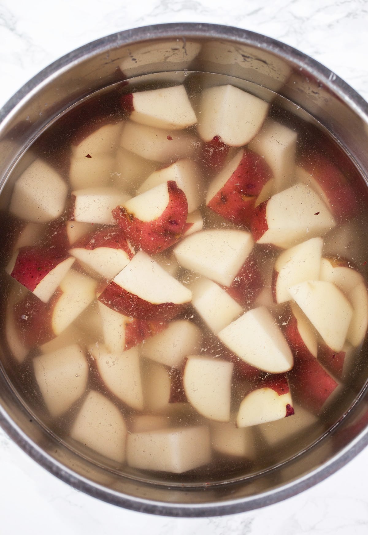 Uncooked diced red potatoes in pot of water.