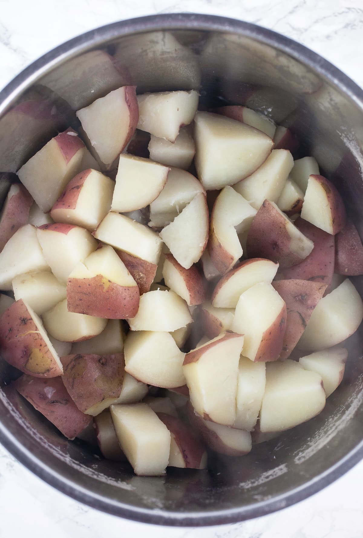 Cooked diced red potatoes in metal pot.