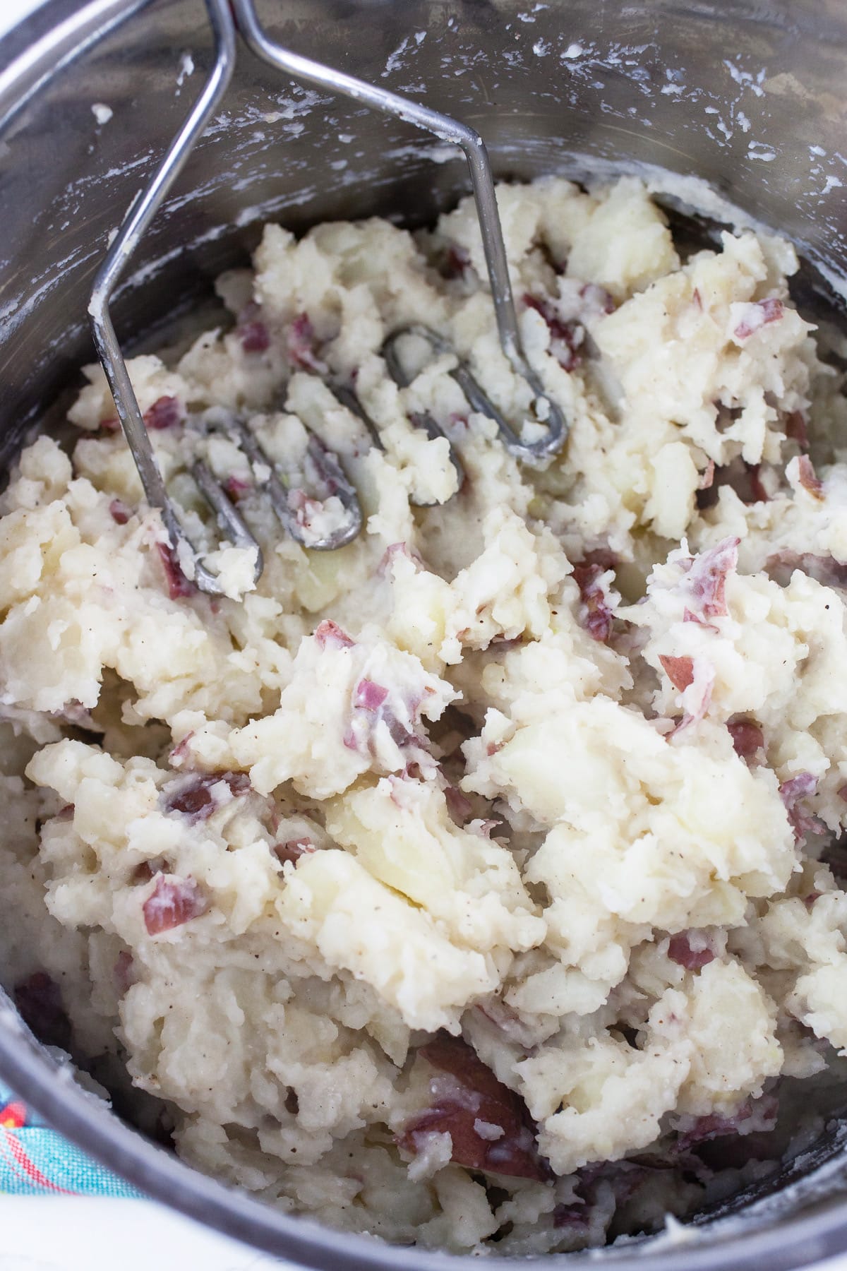 Red potatoes in large pot mashed with potato masher.