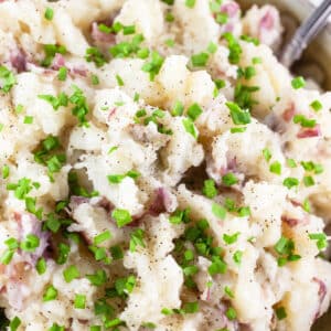 Buttermilk mashed red potatoes with minced chives in ceramic bowl with spoon.