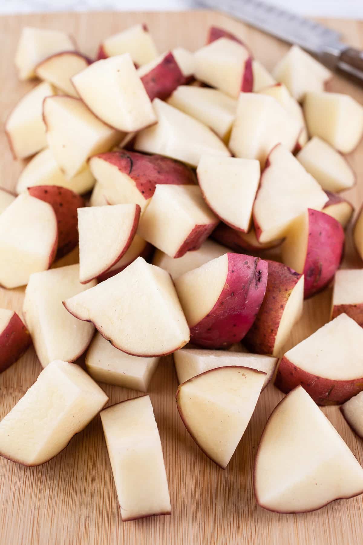 Diced red potatoes on wooden cutting board with knife.