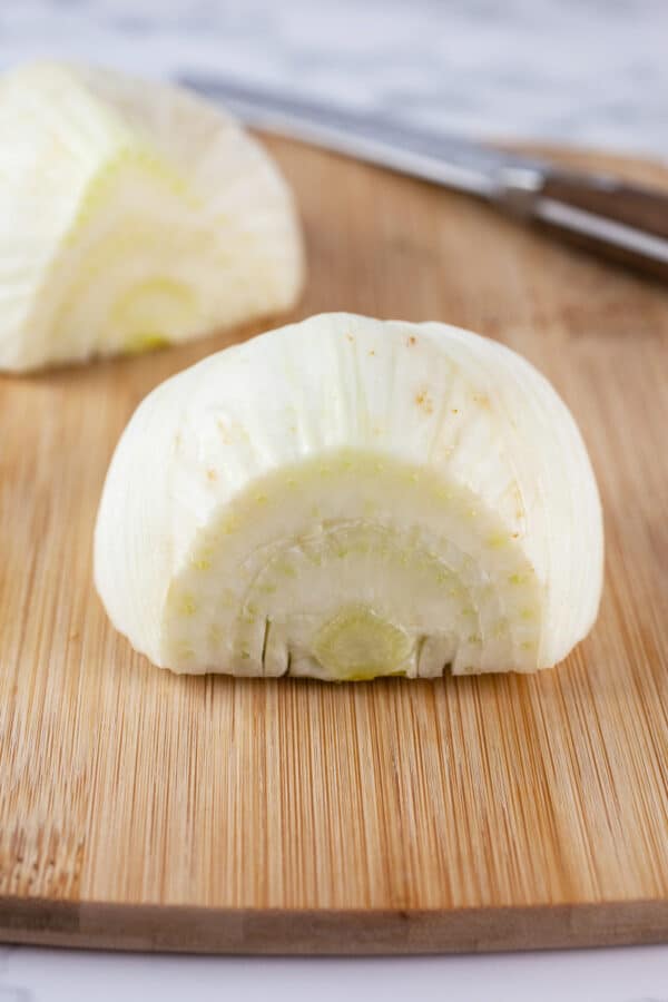 Fennel bulb cut in half on wooden cutting board with knife.