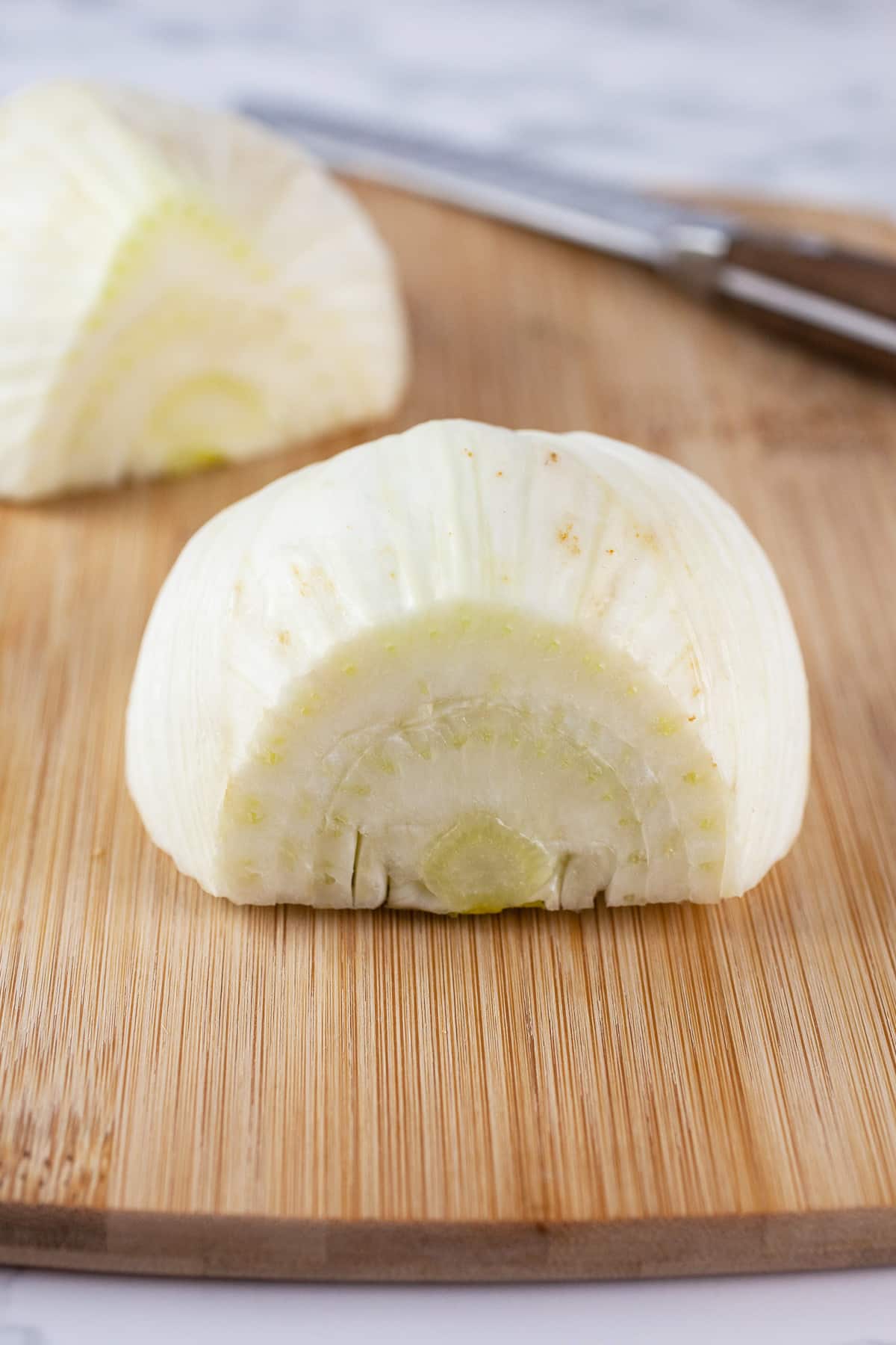 Fennel bulb cut in half on wooden cutting board with knife.