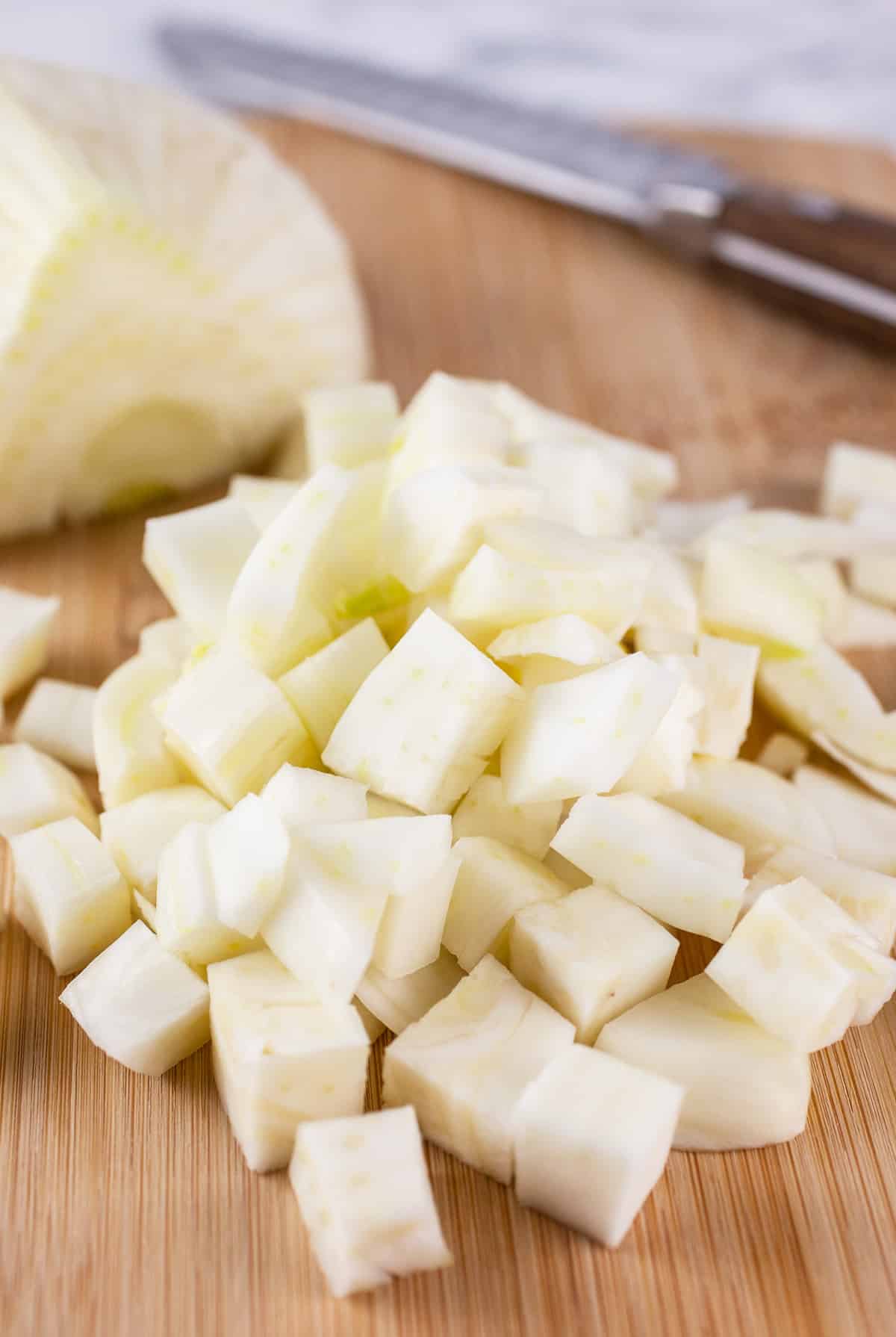 Half of diced fennel bulb on wooden cutting board with knife.