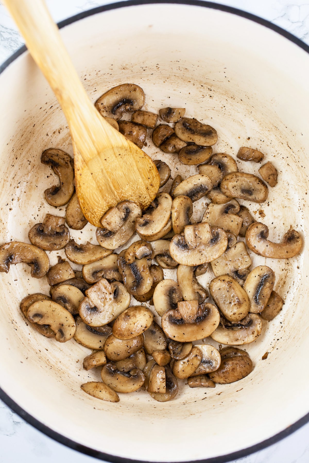 Sliced mushrooms sautéed in Dutch oven with wooden spoon.