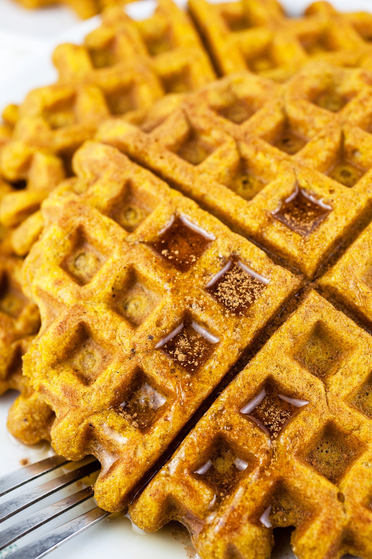 Gluten free pumpkin waffles with maple syrup on white plate.