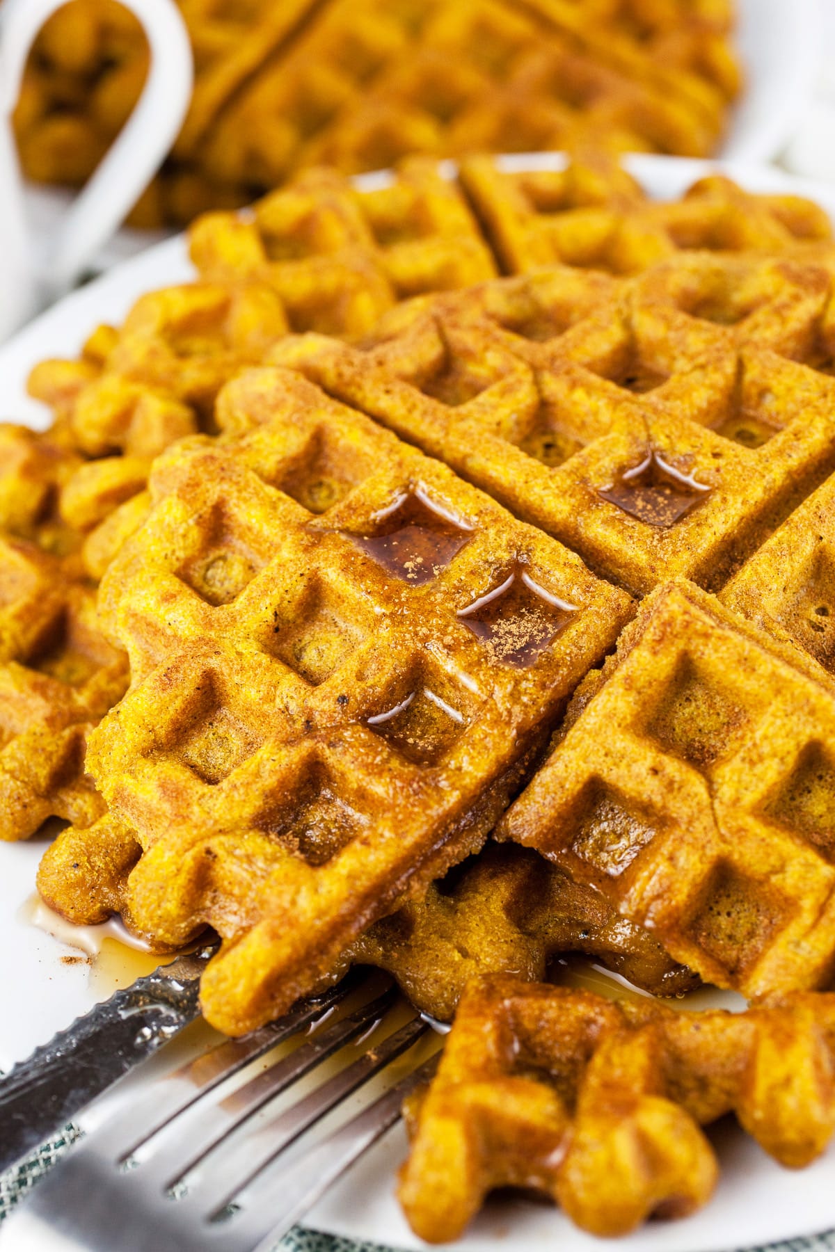 Bite cut from pumpkin waffles on white plate with fork and knife.