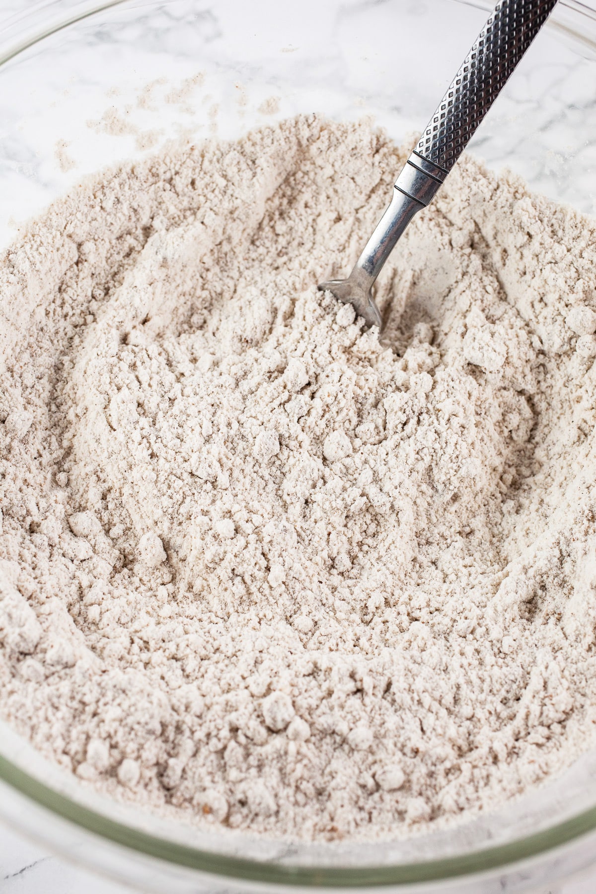 Dry ingredients combined in large glass bowl with fork.