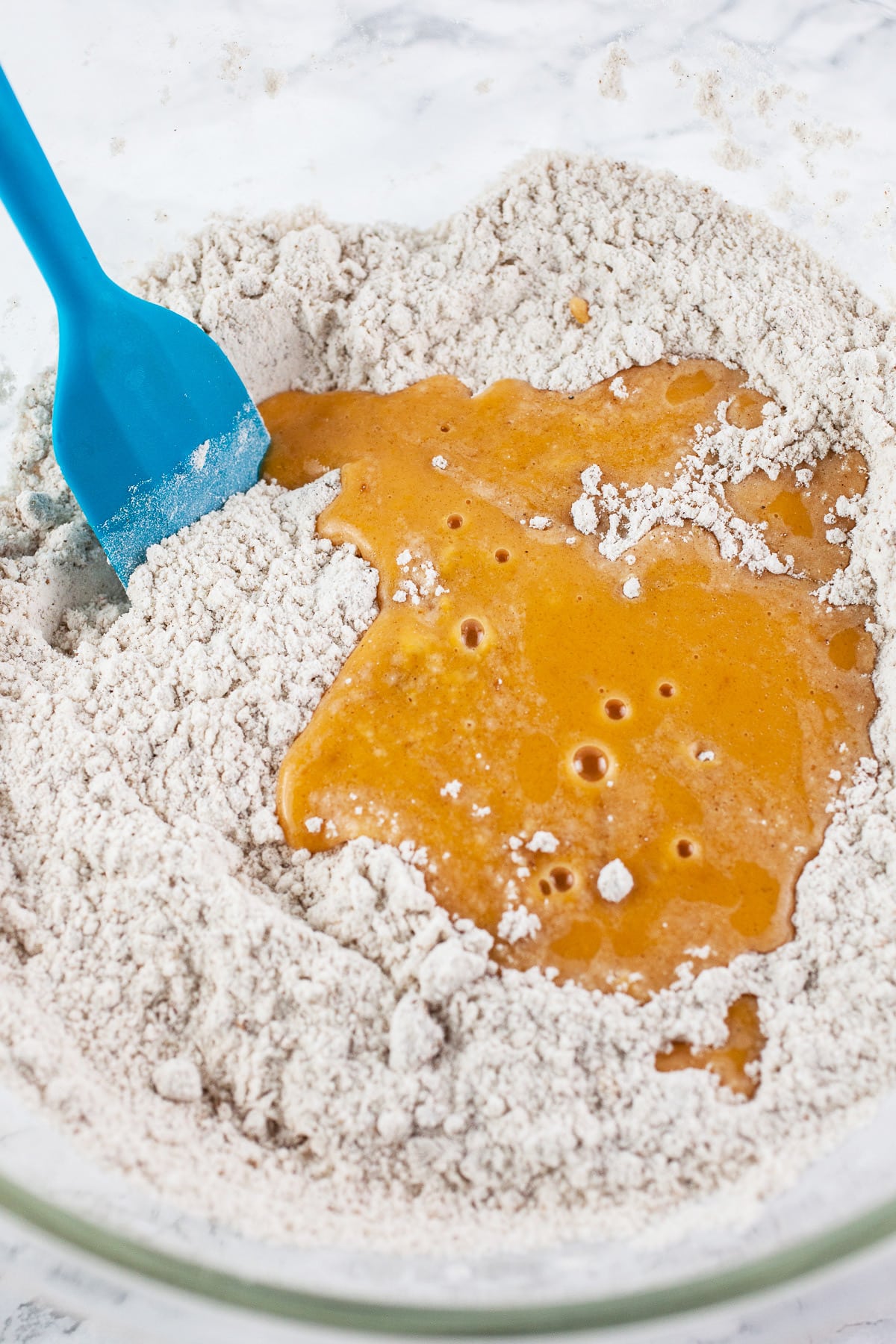 Wet pumpkin waffle ingredients added to dry in large glass bowl with blue spatula.