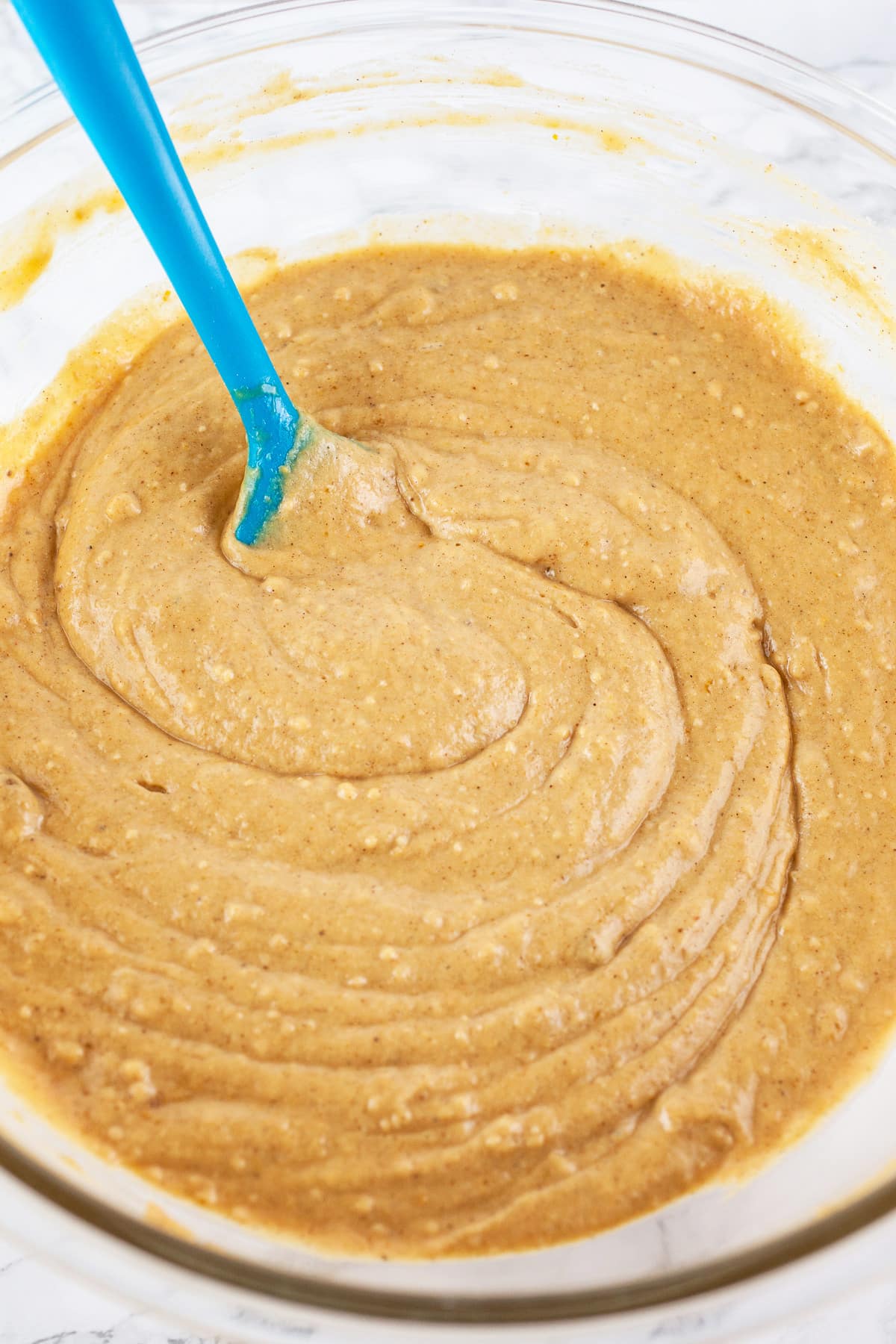 Pumpkin waffle batter in large glass bowl with blue spatula.