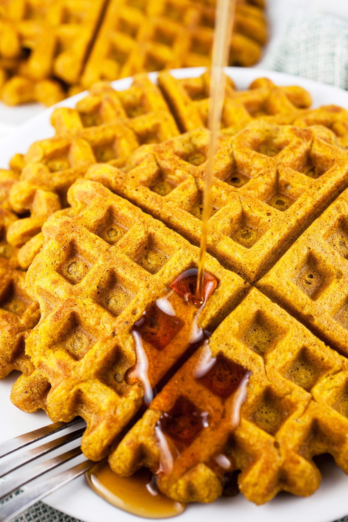 Maple syrup poured over pumpkin waffles on white plate with fork.