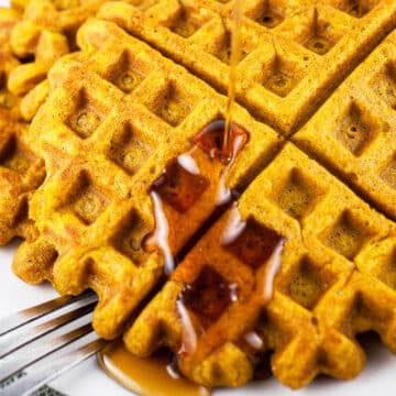 Maple syrup poured onto pumpkin waffles on white plate with fork.