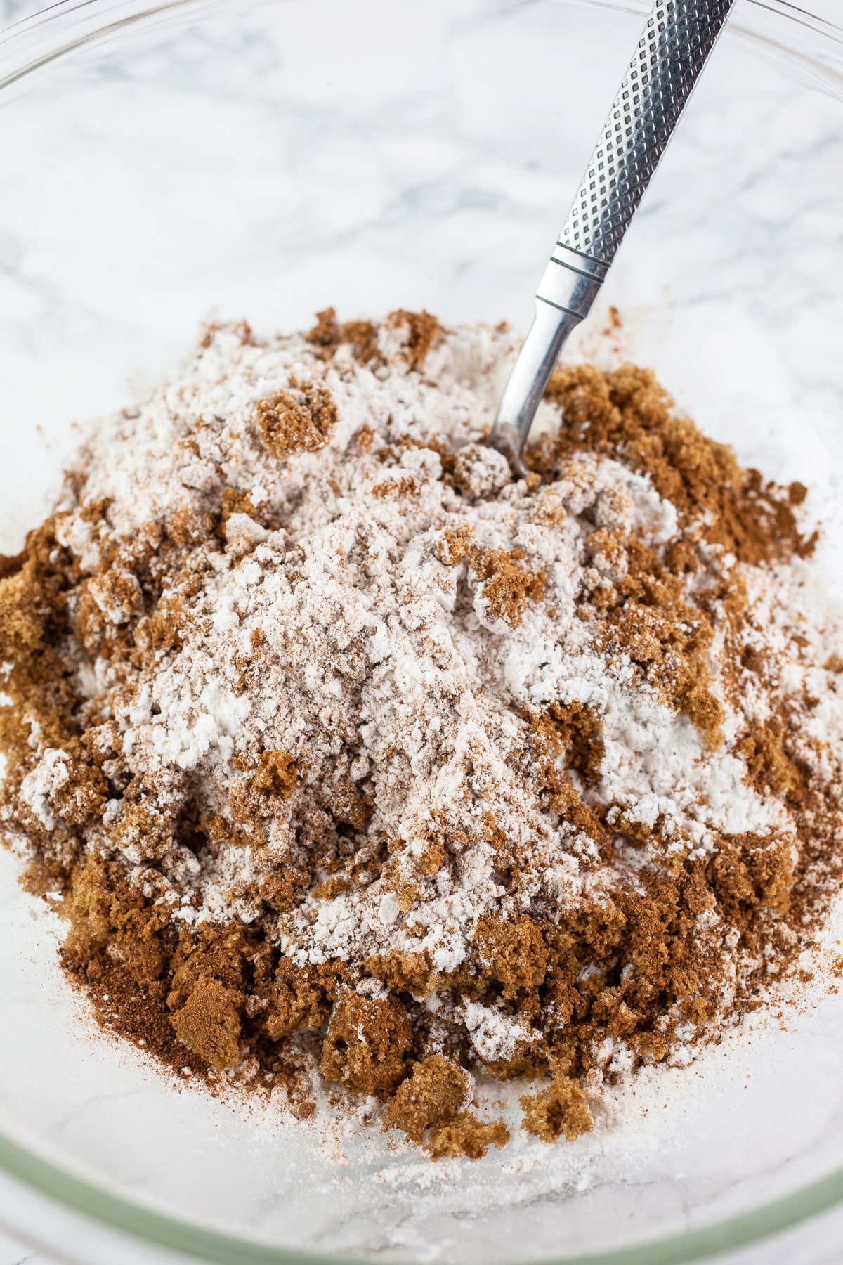 Brown sugar added to dry ingredients in large glass bowl with fork.