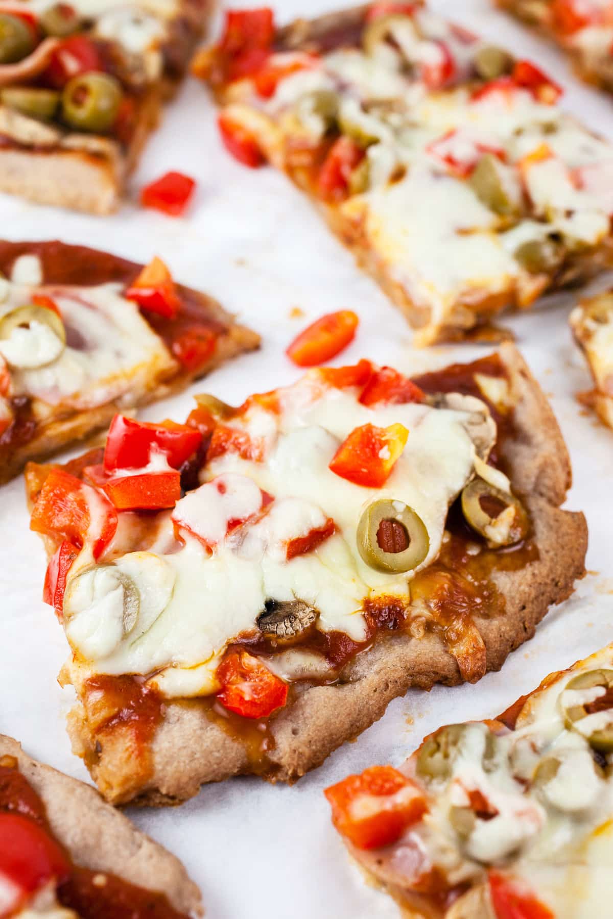 Slices of Canadian bacon pizza with red bell peppers and green olives on white surface.