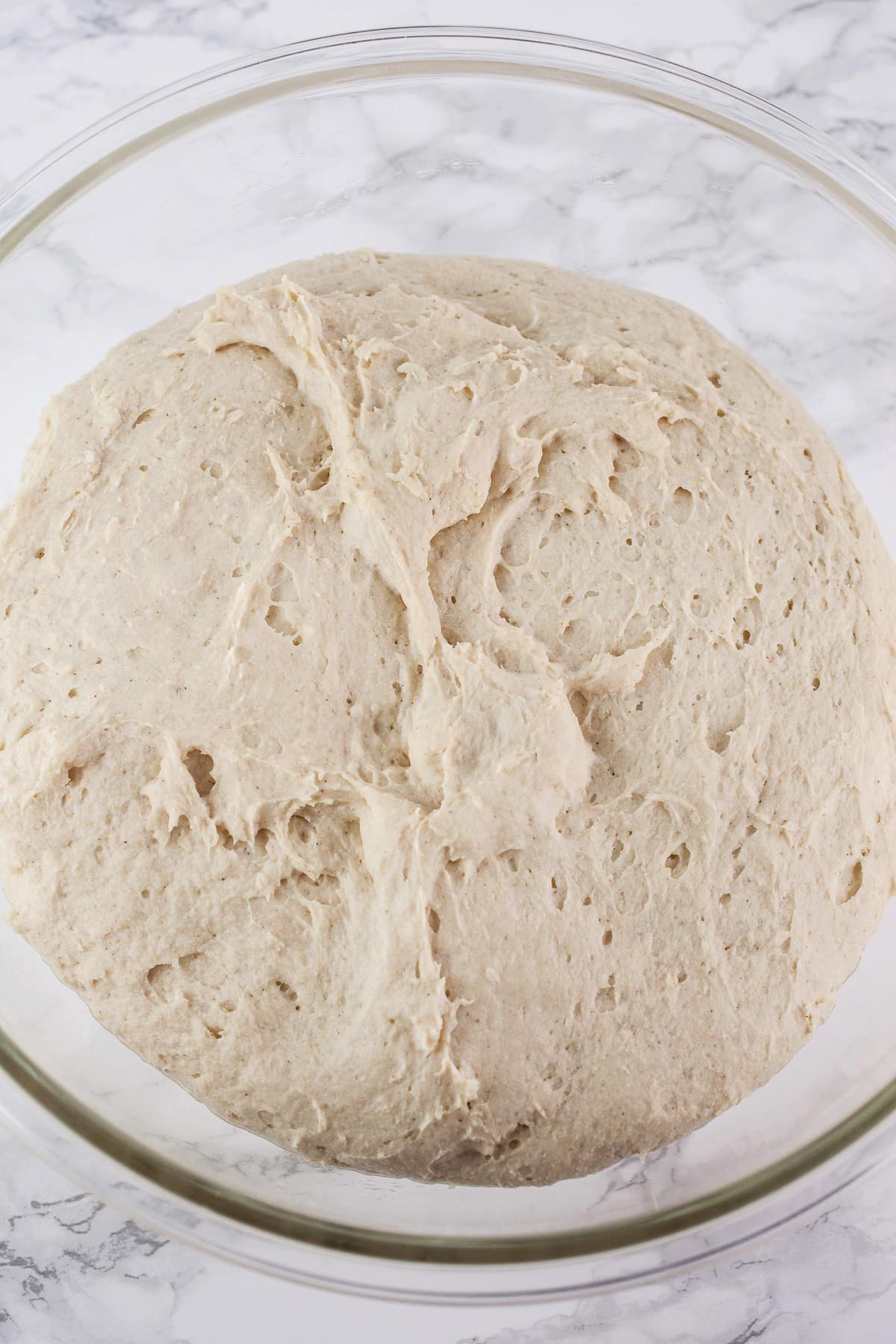 Risen pizza dough in large glass bowl.