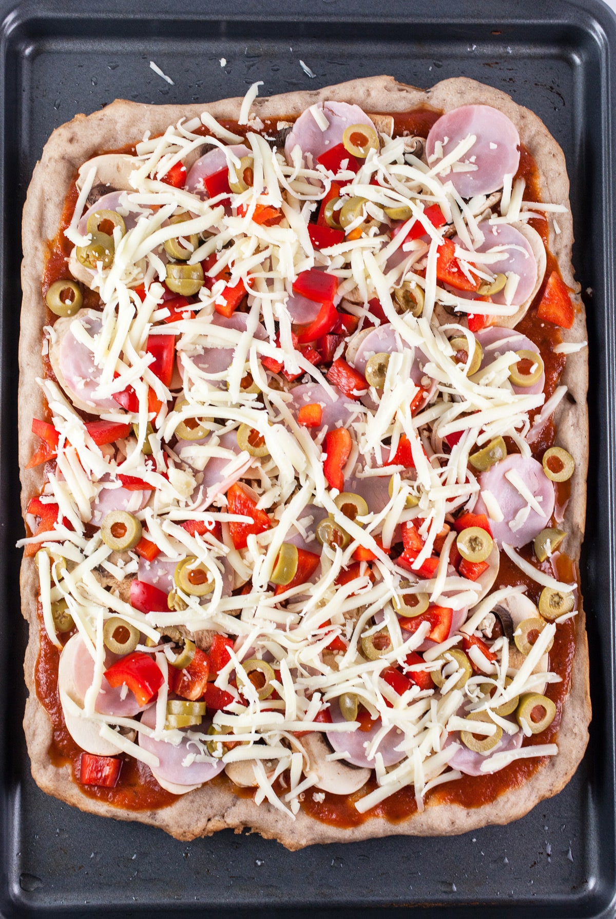 Uncooked pizza with toppings on baking sheet.