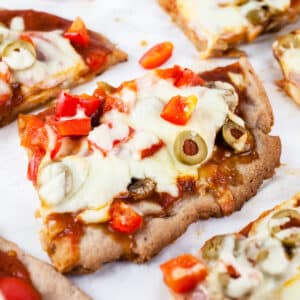 Slices of Canadian bacon pizza with red bell peppers and olives on white surface.