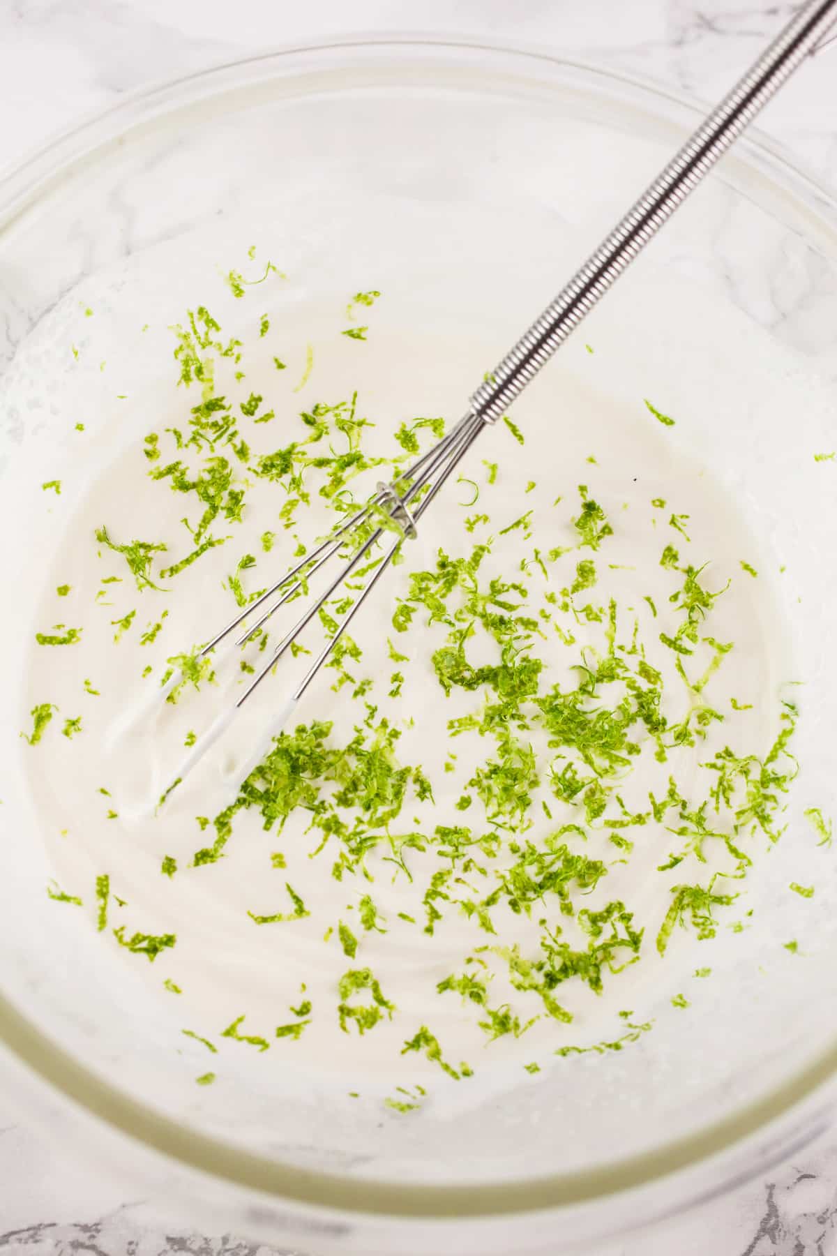 Mexican crema with lime zest in glass bowl with small whisk.