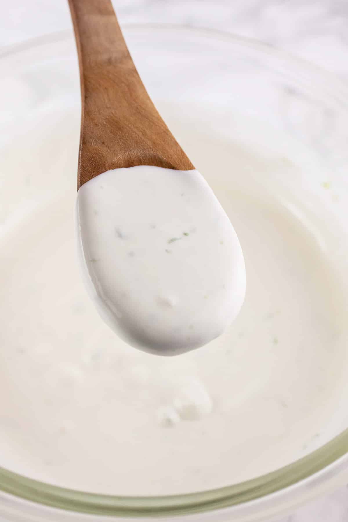 Wooden spoonful of Mexican crema lifted from small glass bowl.