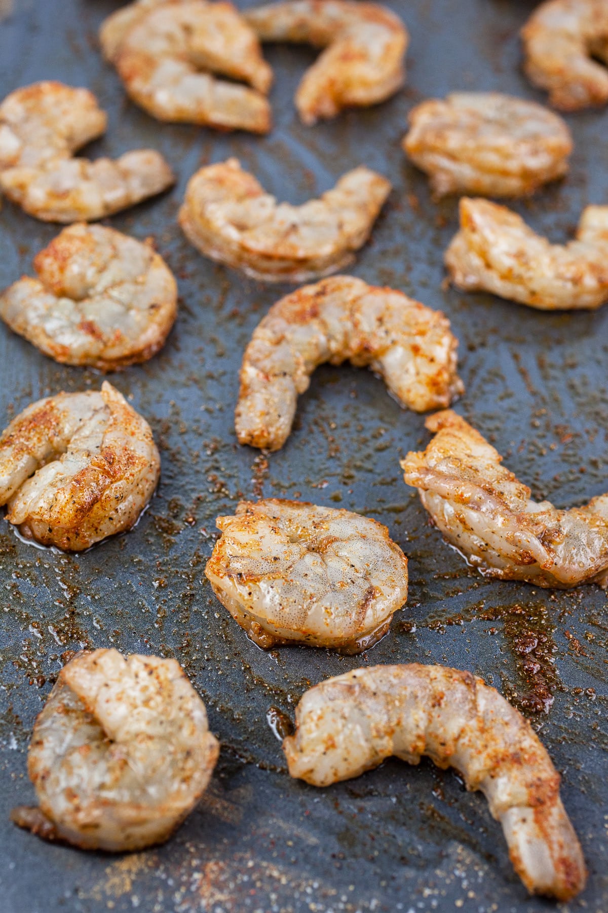 Raw shrimp tossed with olive oil and spices on baking sheet.