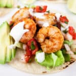 Sheet pan shrimp taco with sliced avocado and lime crema on corn tortilla.