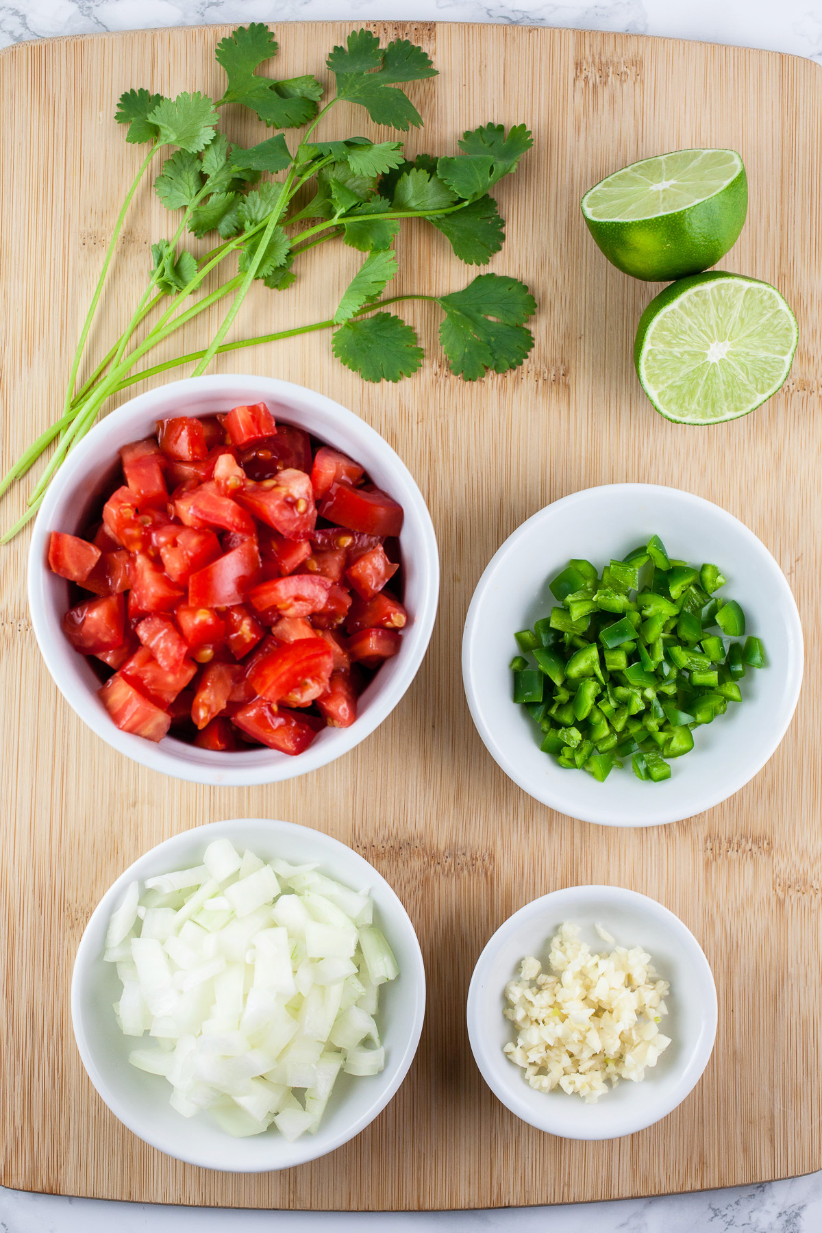 Minced garlic, onions, jalapeno, tomatoes, cilantro, and lime on wooden cutting board.