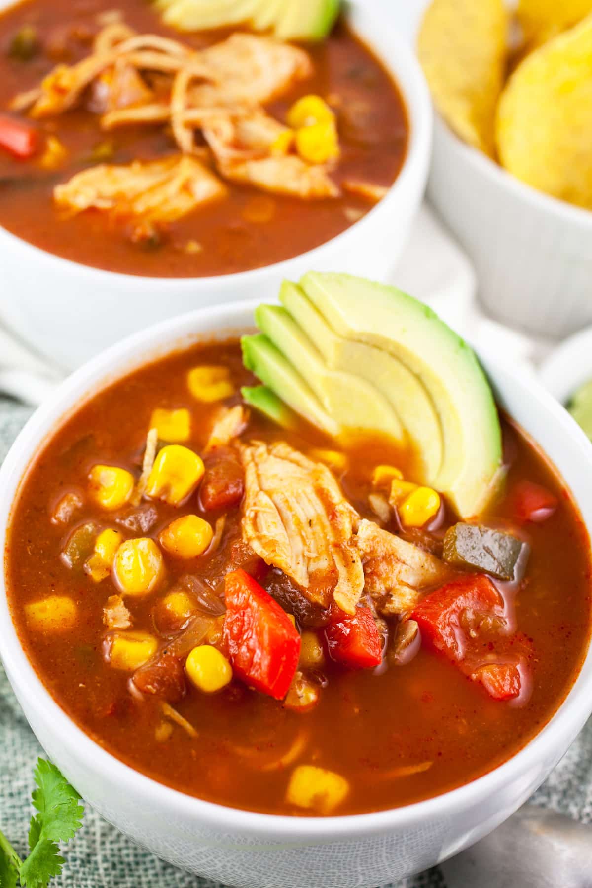 Chicken corn soup in white bowls with sliced avocado and tortilla chips.