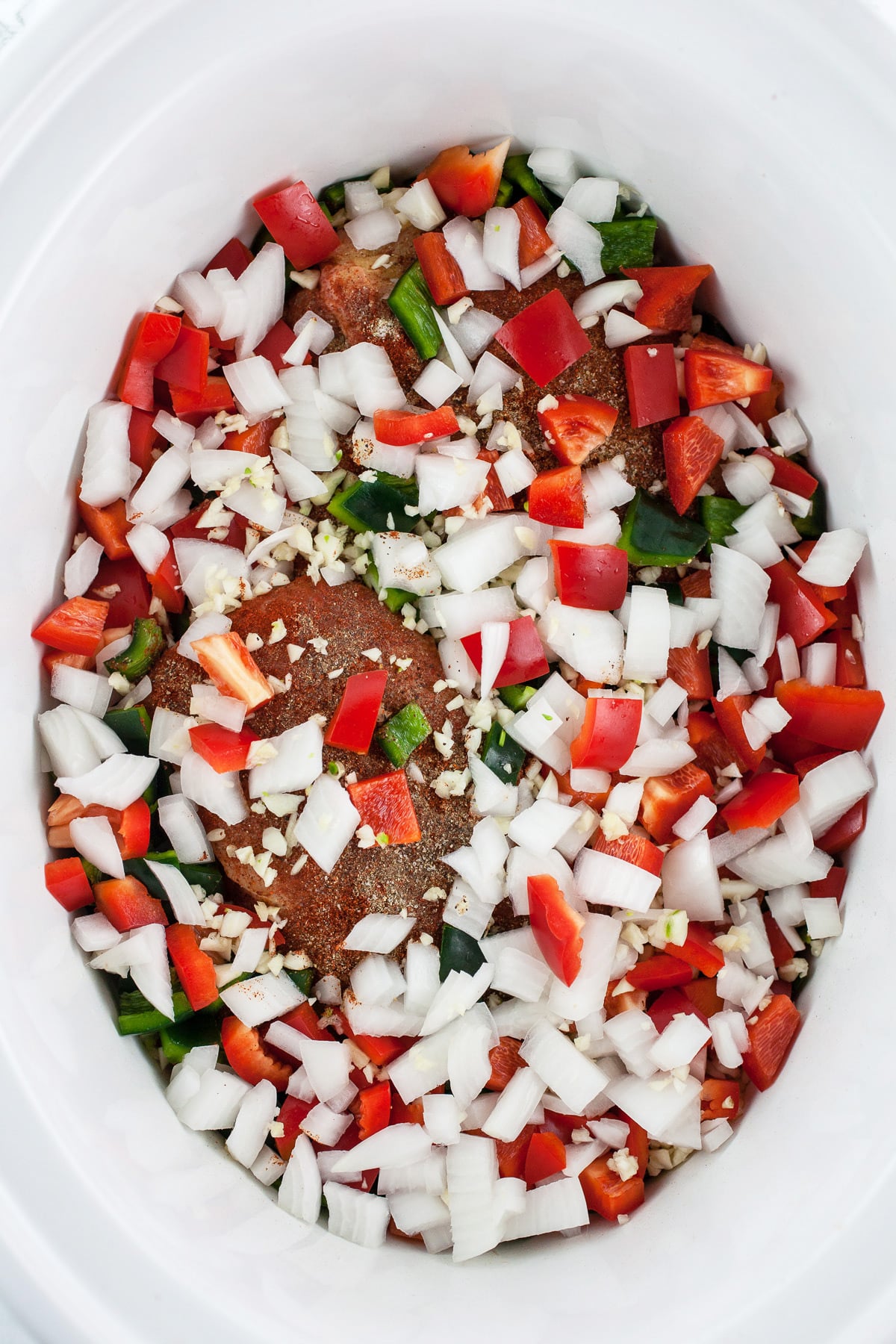 Split chicken breasts with spices, garlic, onions, and diced peppers in slow cooker.