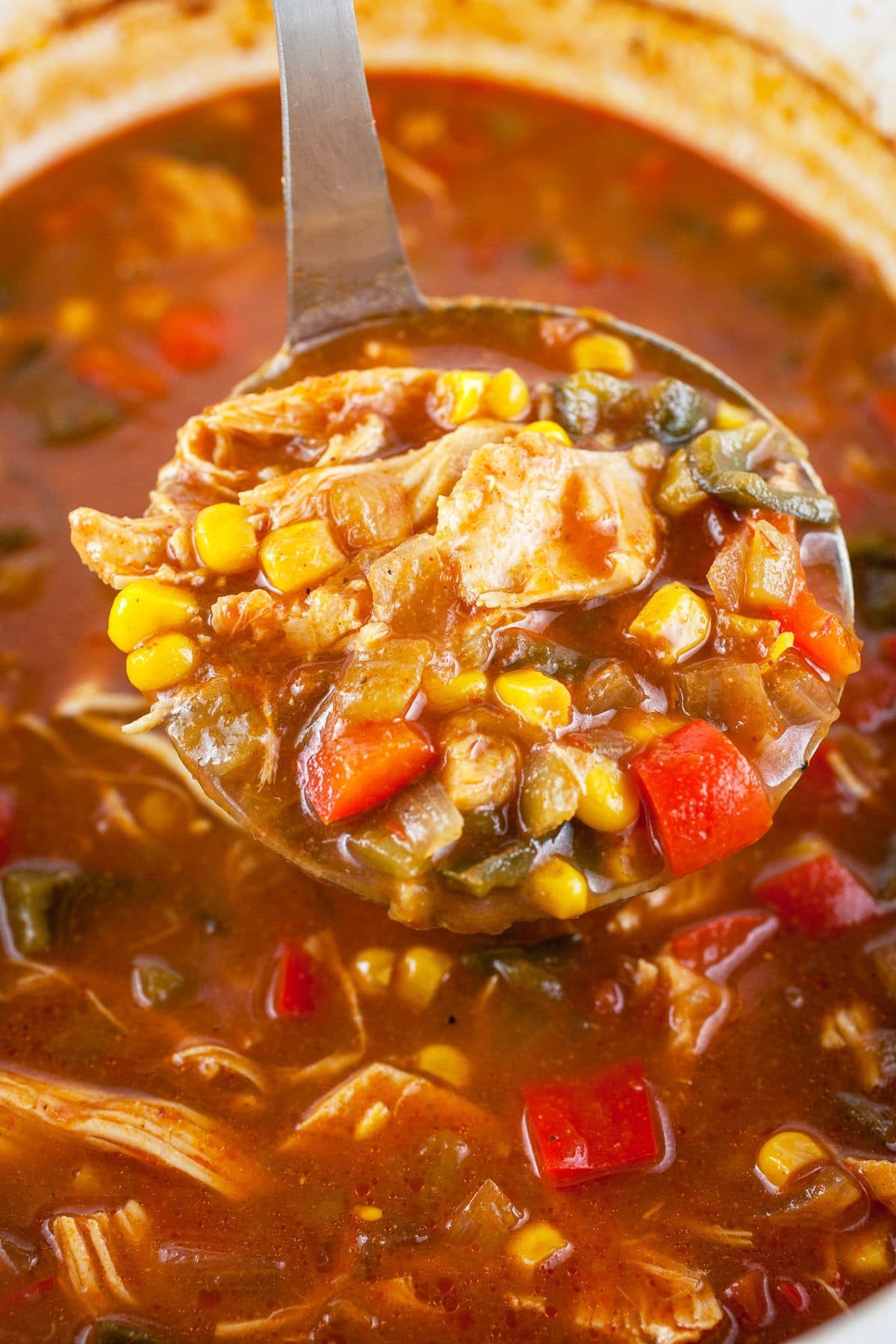 Scoop of chicken corn soup lifted from slow cooker on metal ladle.