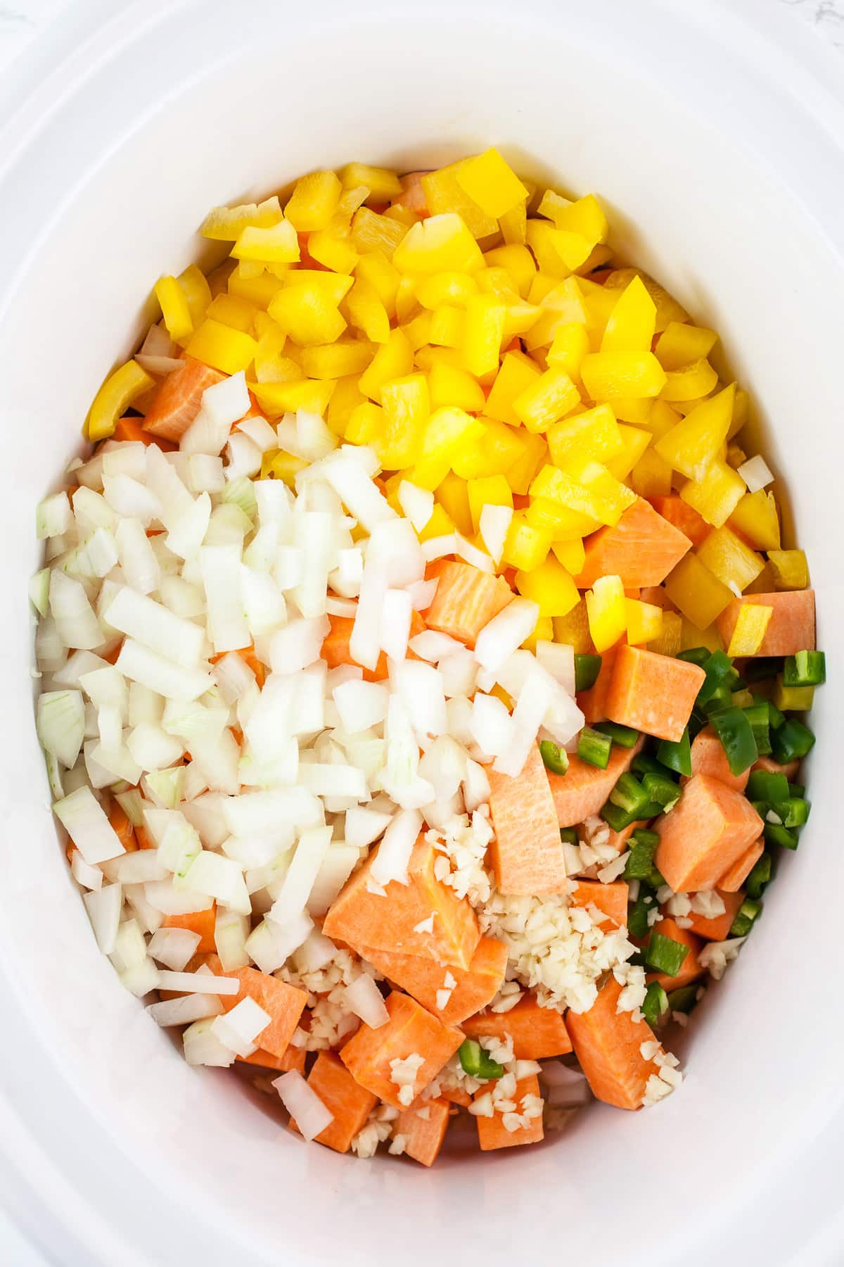 Minced garlic, onions, jalapeno pepper, yellow bell pepper, and sweet potatoes in slow cooker.