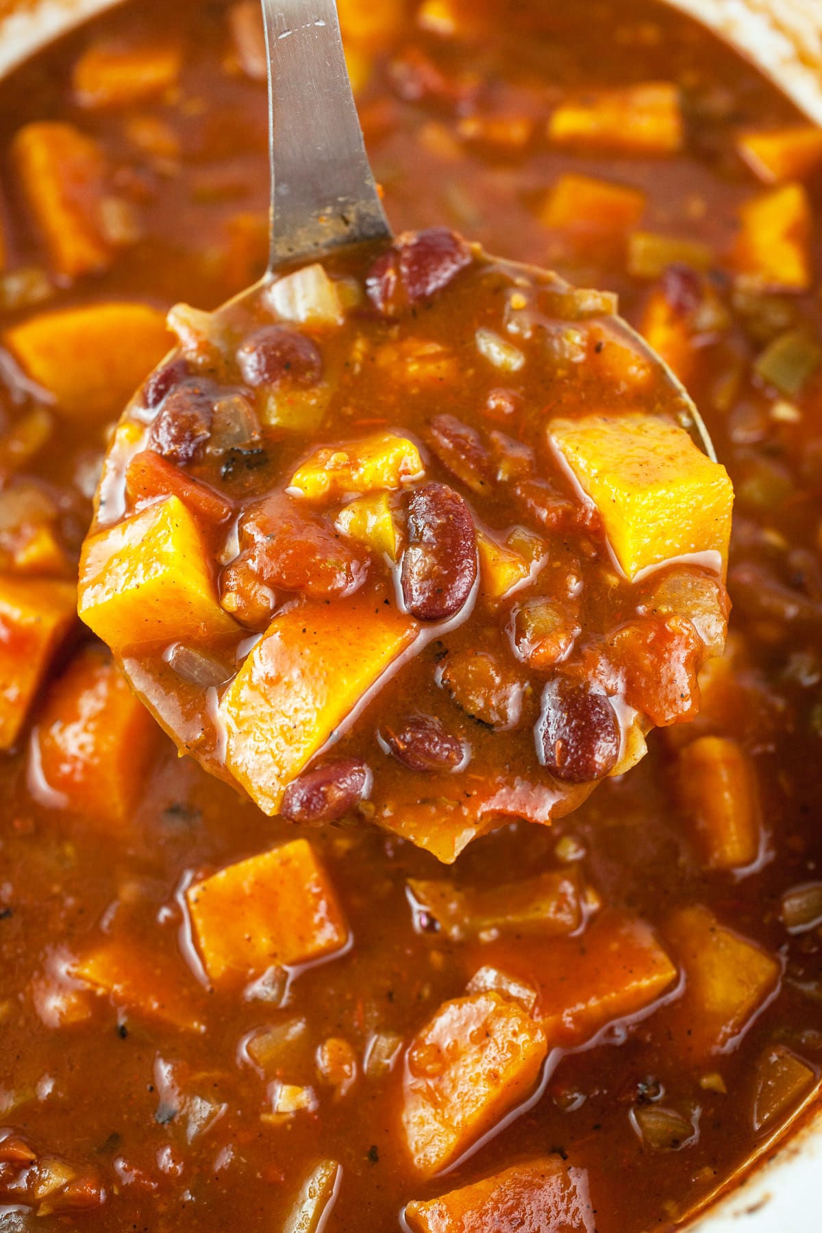 Scoop of vegan chili lifted from crockpot on metal ladle.