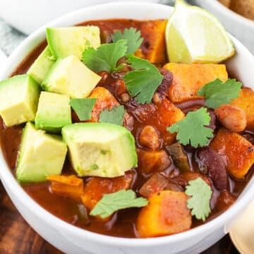 Slow cooker veggie chili with diced avocado, cilantro, and lime wedge in white bowl.