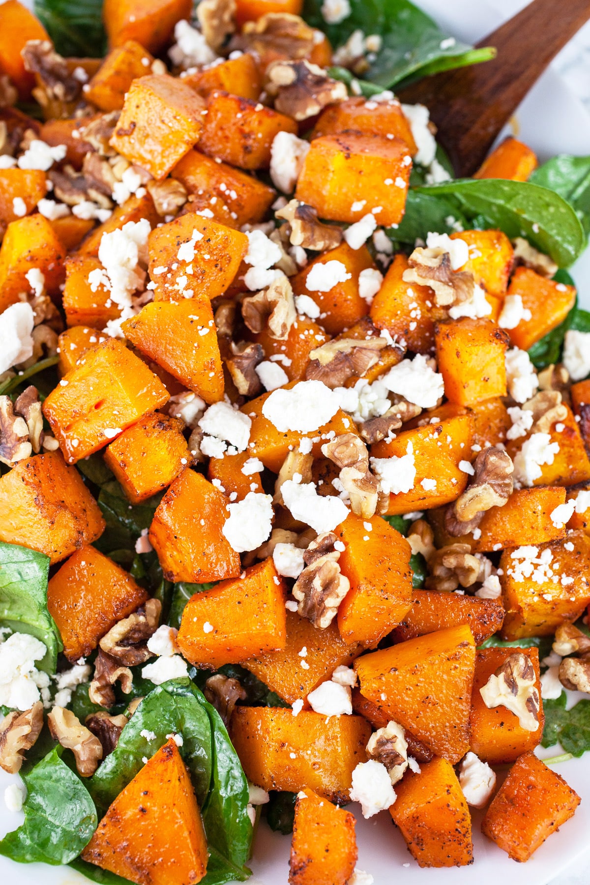 Butternut squash salad with greens, walnuts, and feta on white platter.