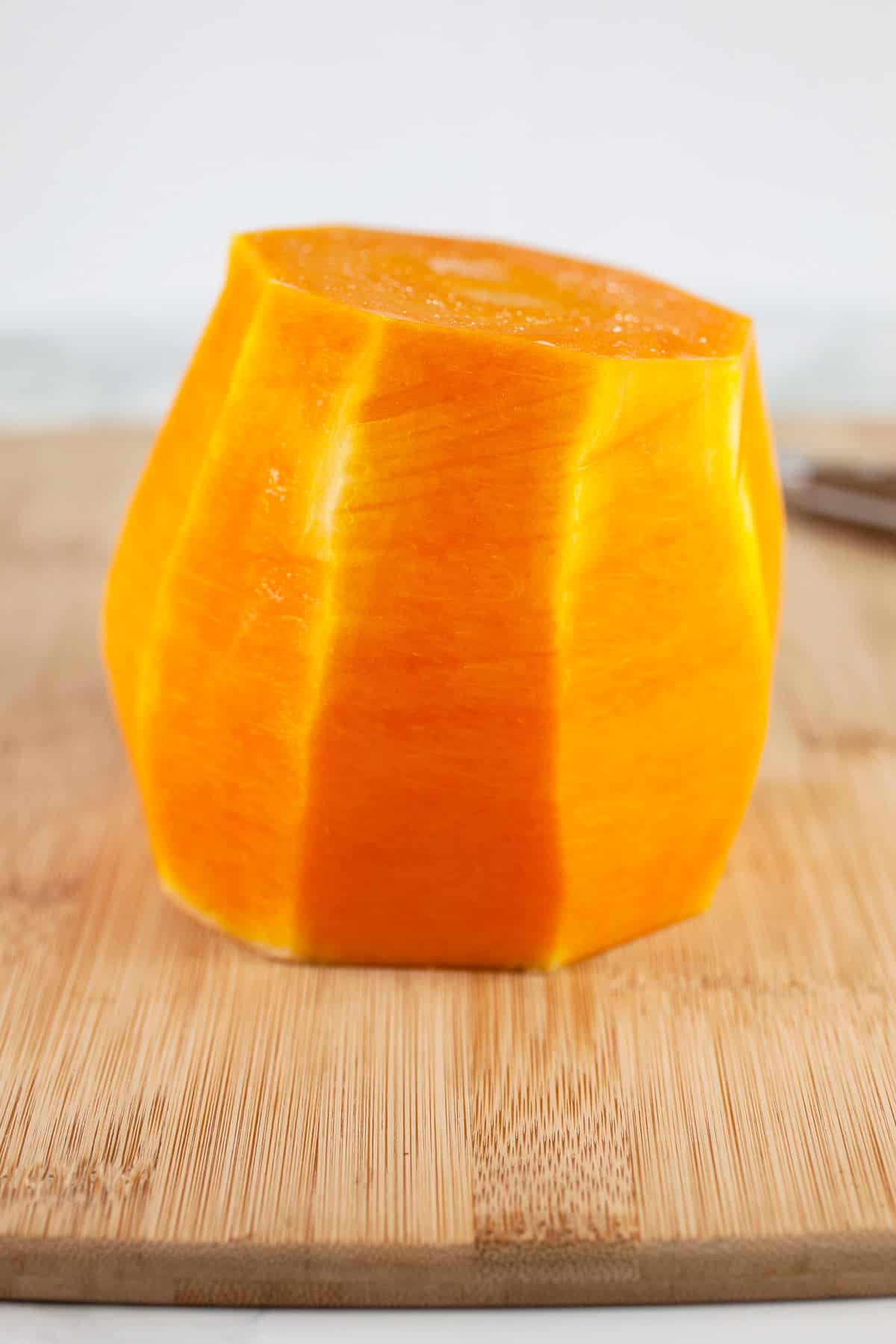 Half of a peeled butternut squash on wooden cutting board.