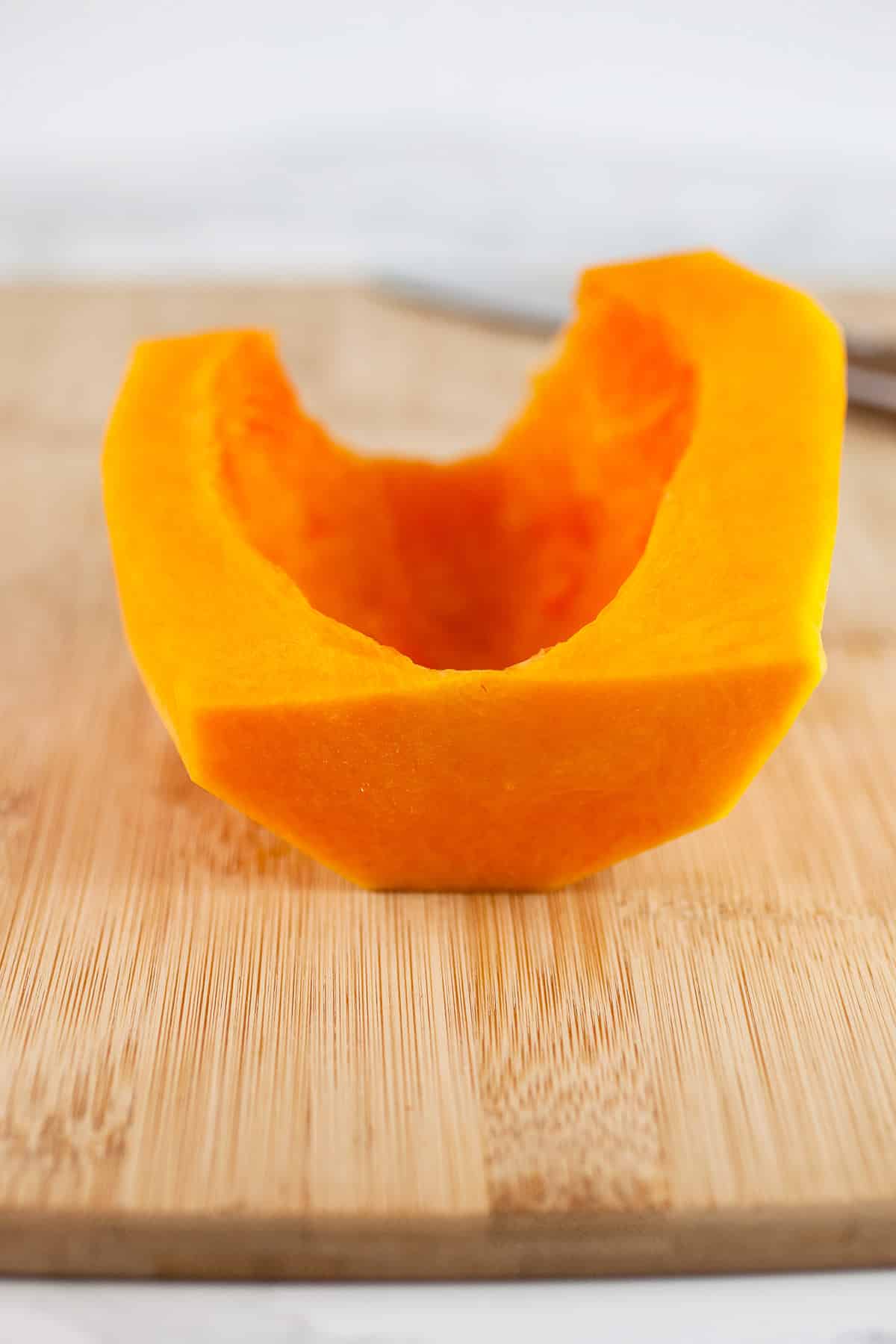 Bottom portion of a butternut squash cut in half with seeds and membranes removed on wooden cutting board.