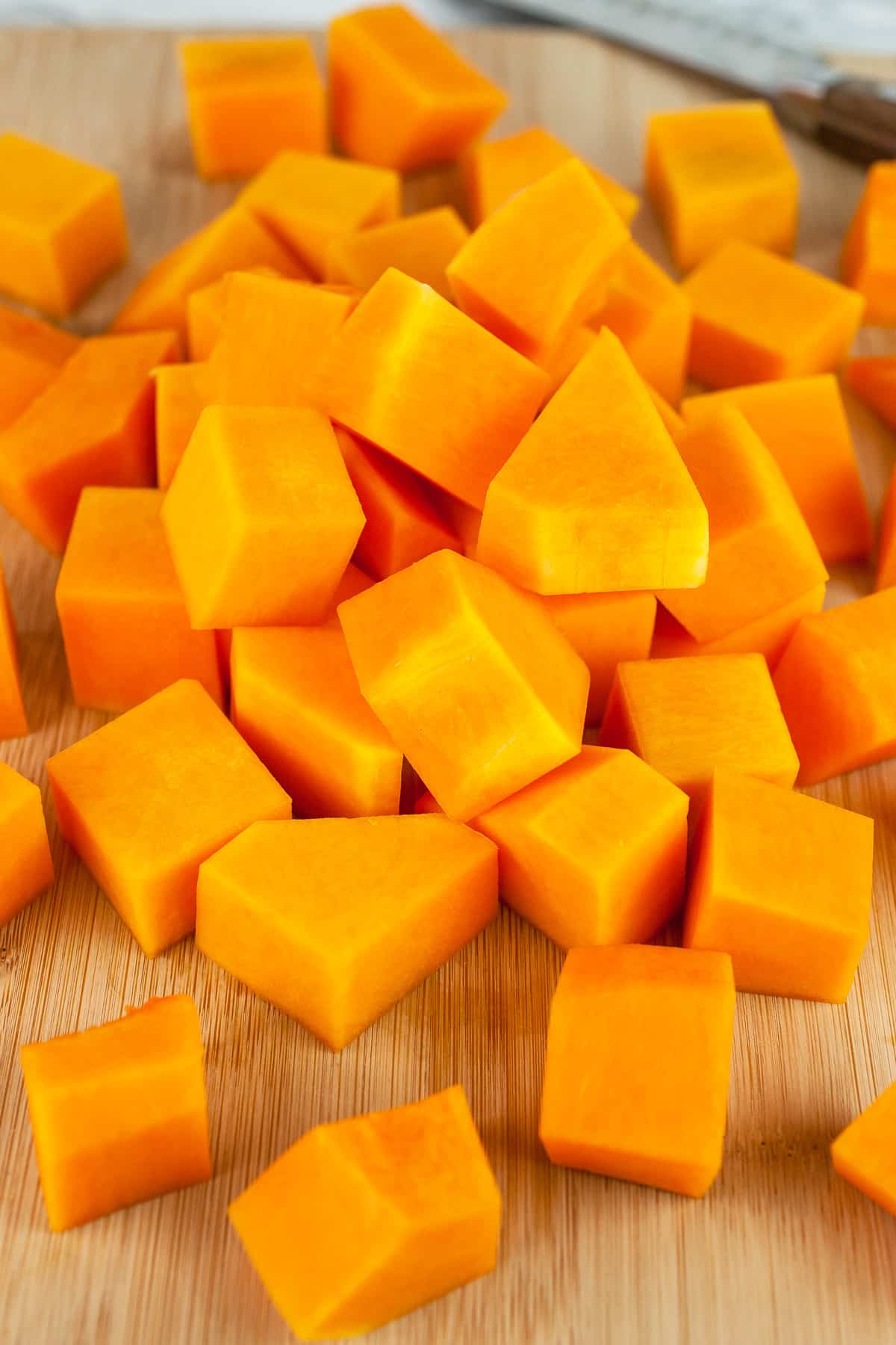 Cubed butternut squash on wooden cutting board with knife.