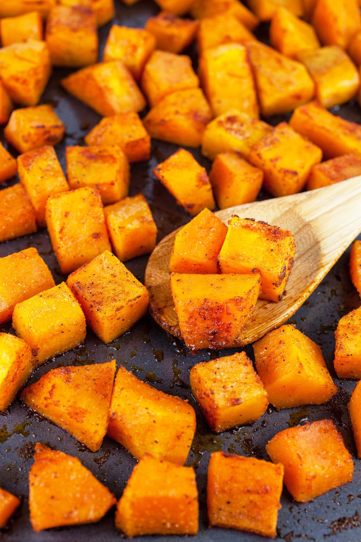 Roasted spiced butternut squash cubes on baking sheet with wooden spoon.