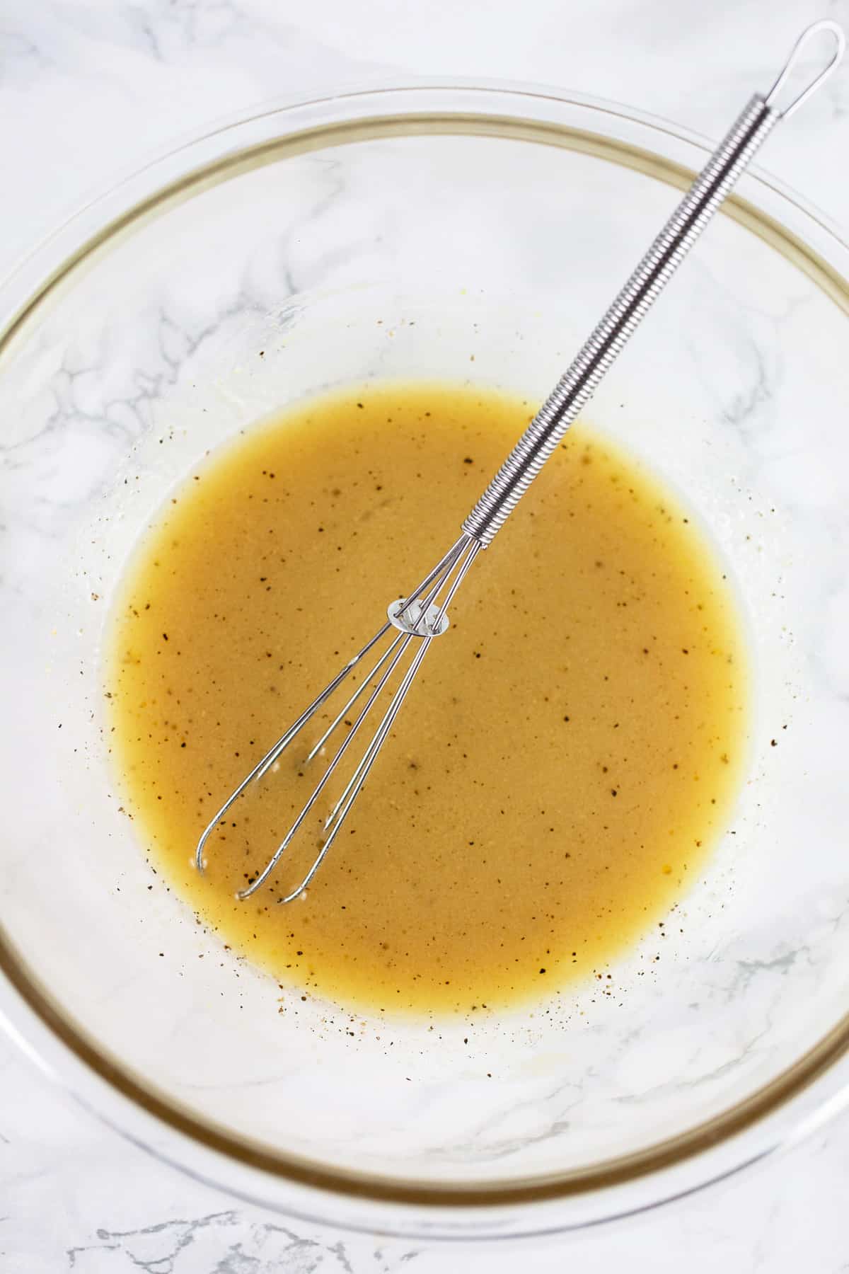 Maple Dijon dressing in small glass bowl with whisk.