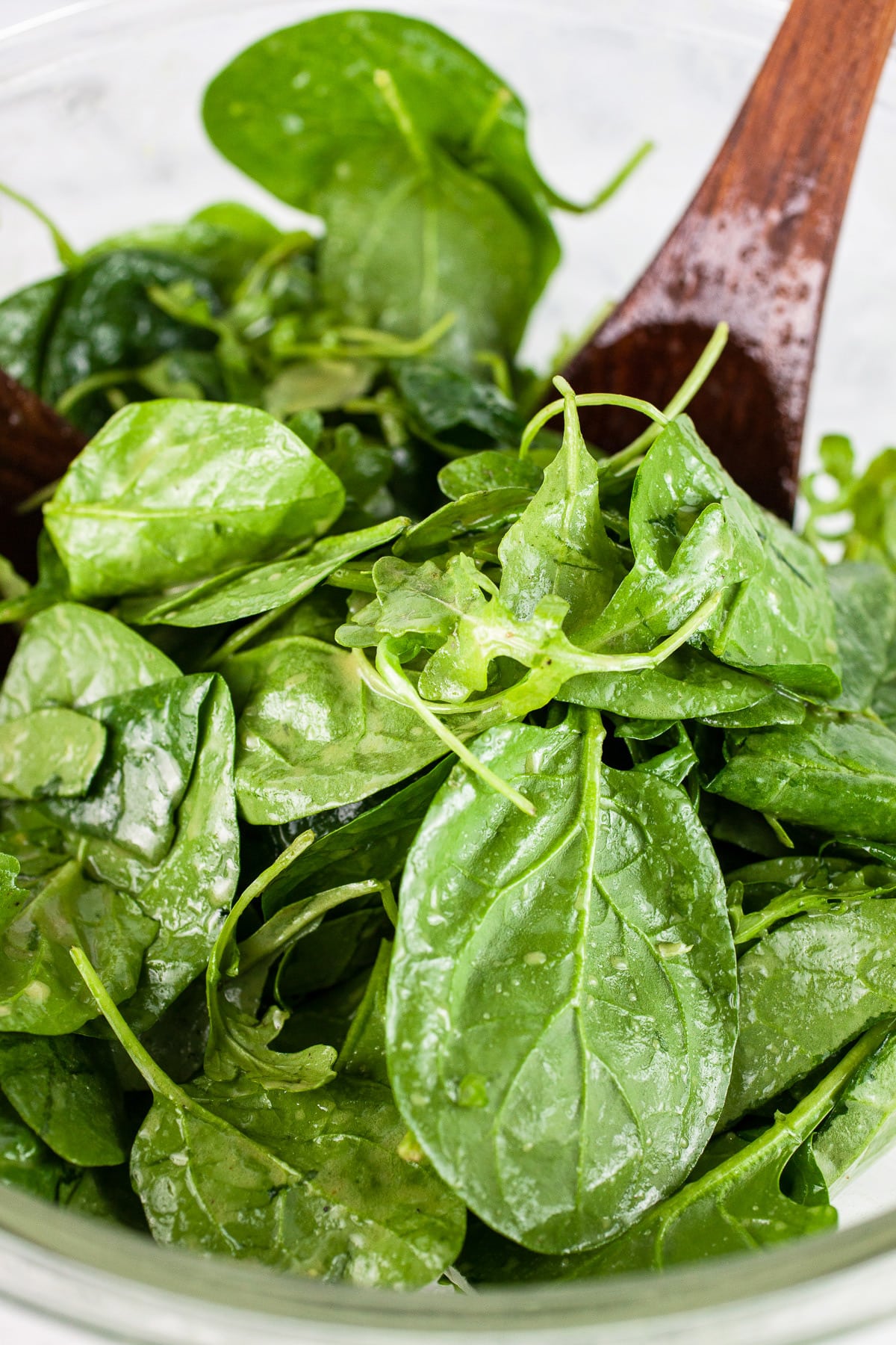 Spinach and arugula tossed with dressing in large glass bowl.