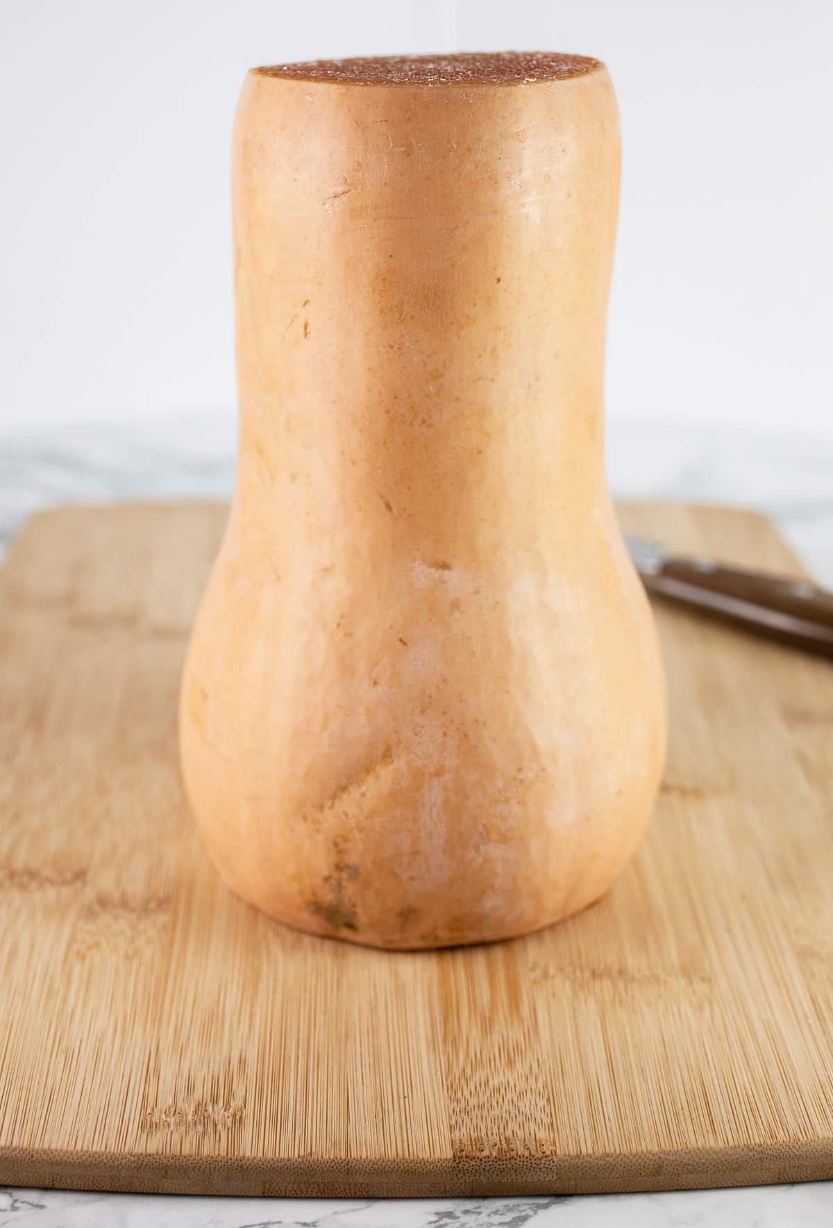 Butternut squash with top and bottom removed on wooden cutting board.