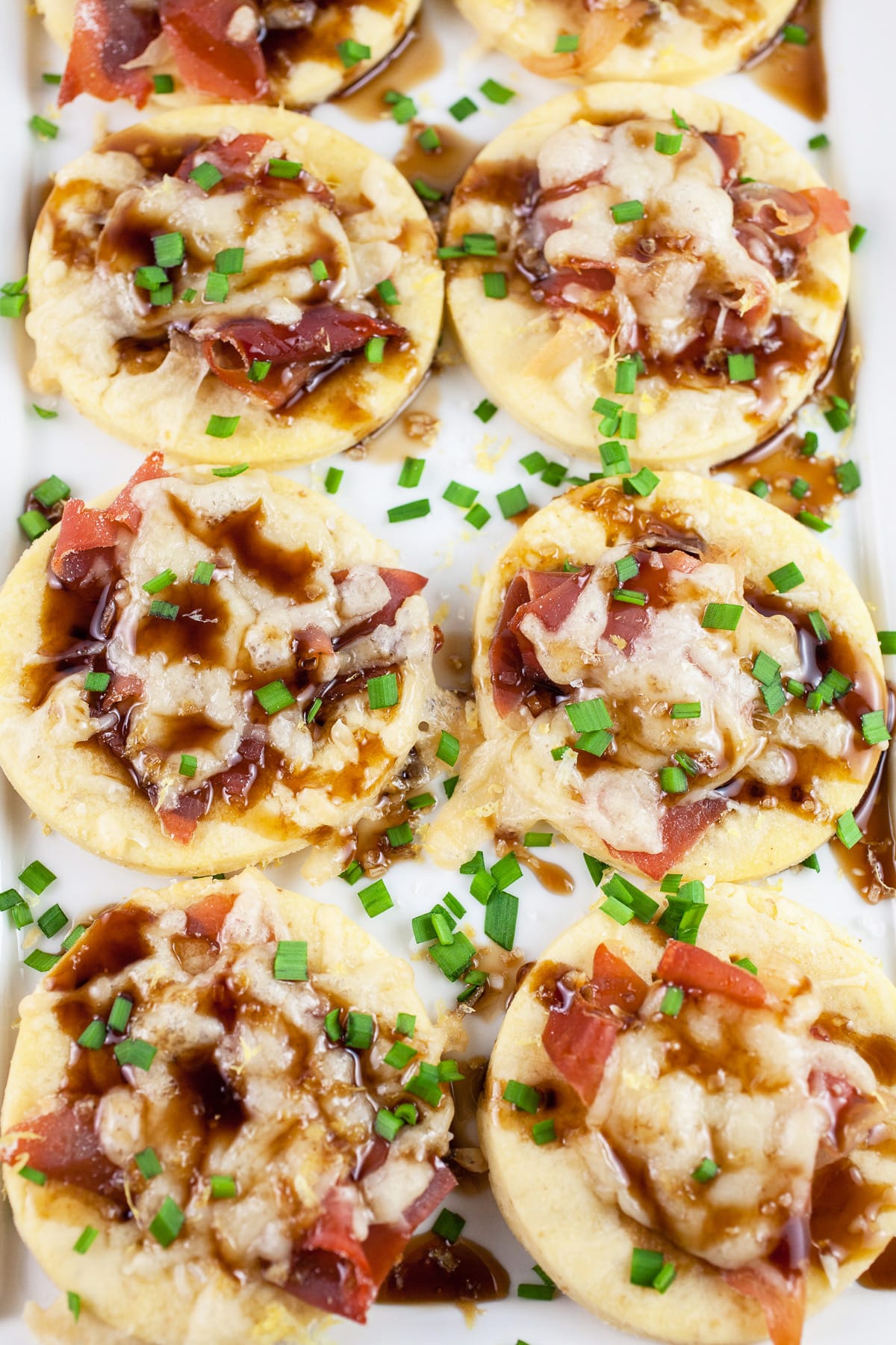 Gruyere prosciutto tartlets with balsamic glaze and minced chives on white platter.