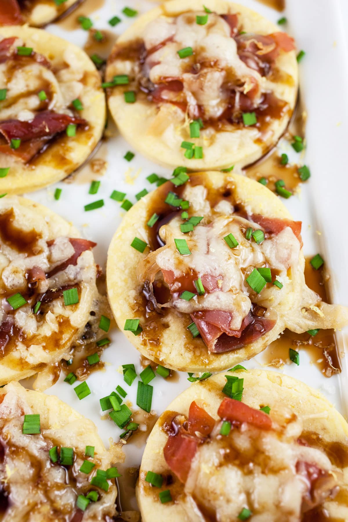 Gruyere prosciutto tartlets with balsamic glaze and minced chives on white platter.