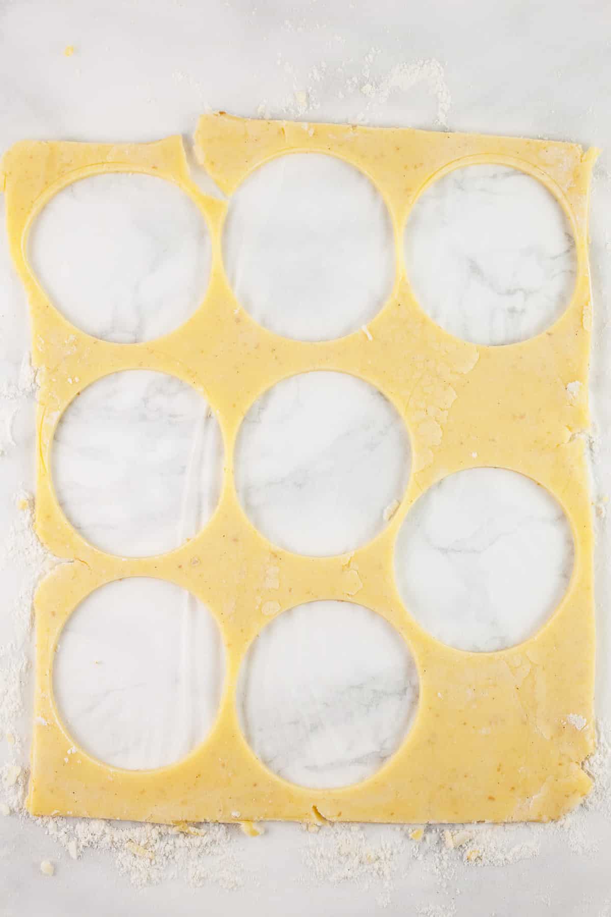 Rounds cut from sheet of gluten free puff pastry on white surface.