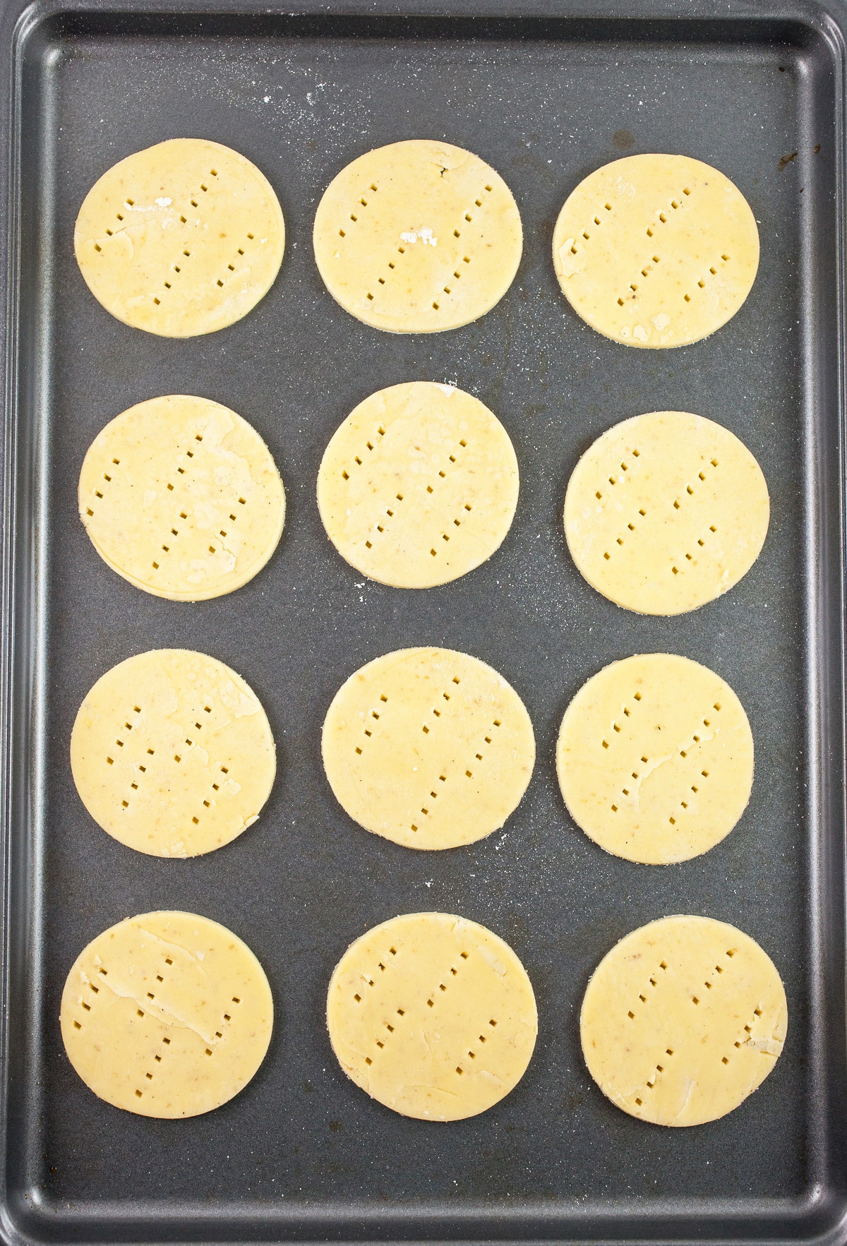 Gluten free puff pastry rounds poked with a fork on baking sheet.